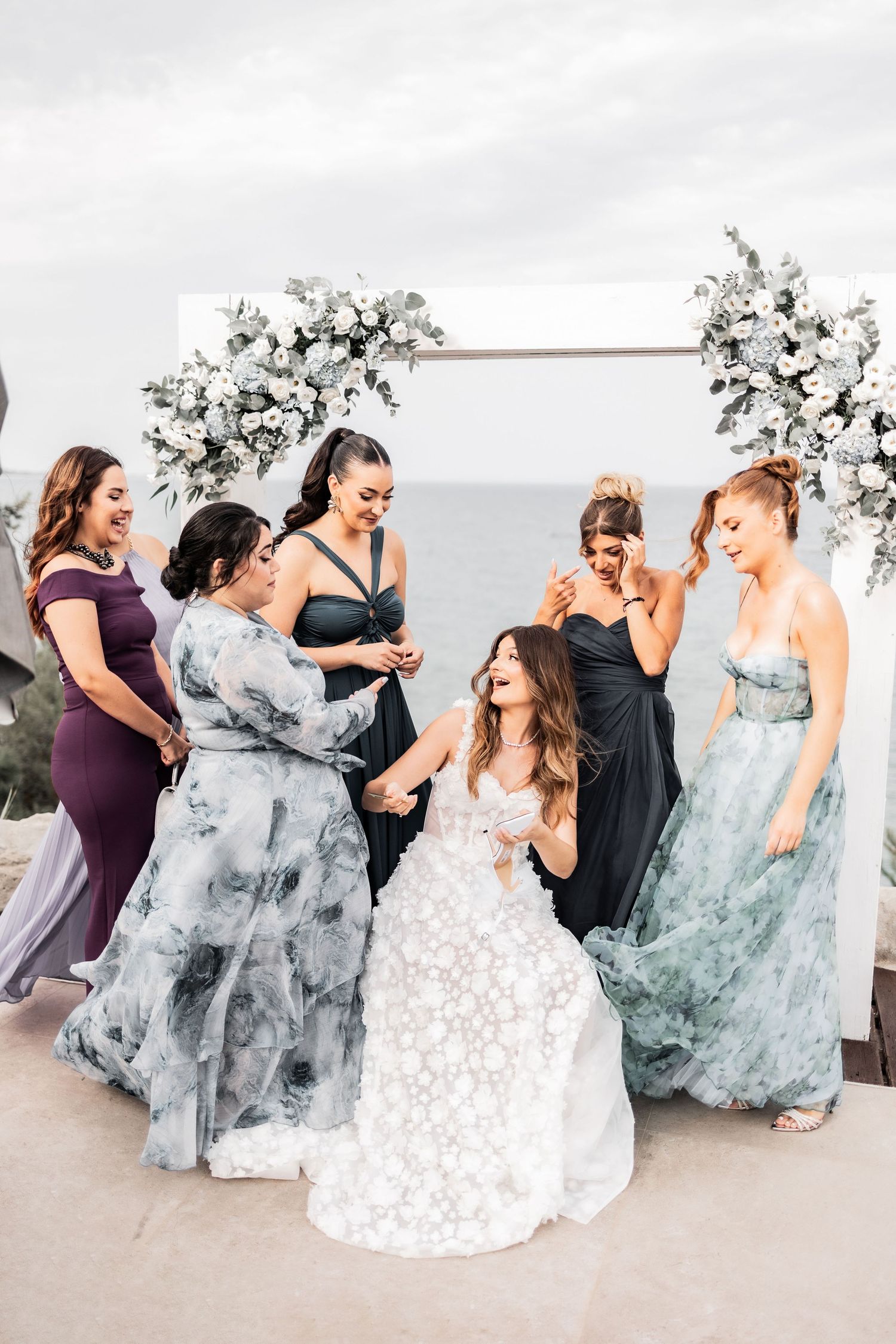 Bridesmaids in flowing blue dresses dance and twirl together at an outdoor venue.