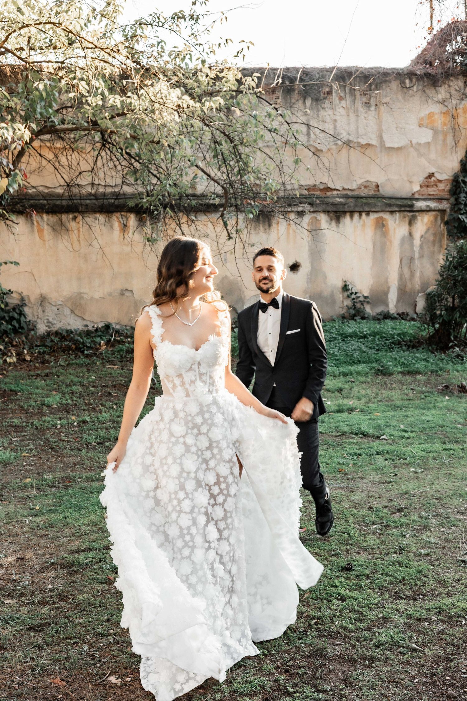 Elegant white floral wedding dress flowing in the breeze against garden backdrop.