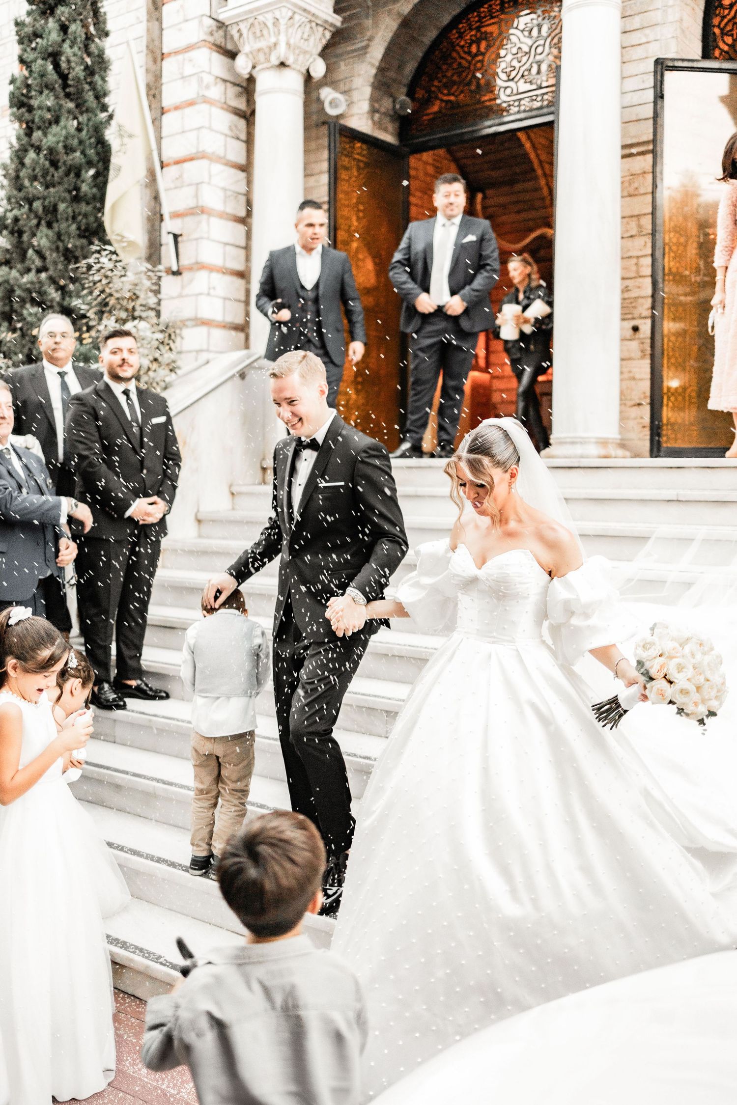 Wedding party celebration outside a grand building with confetti being thrown.