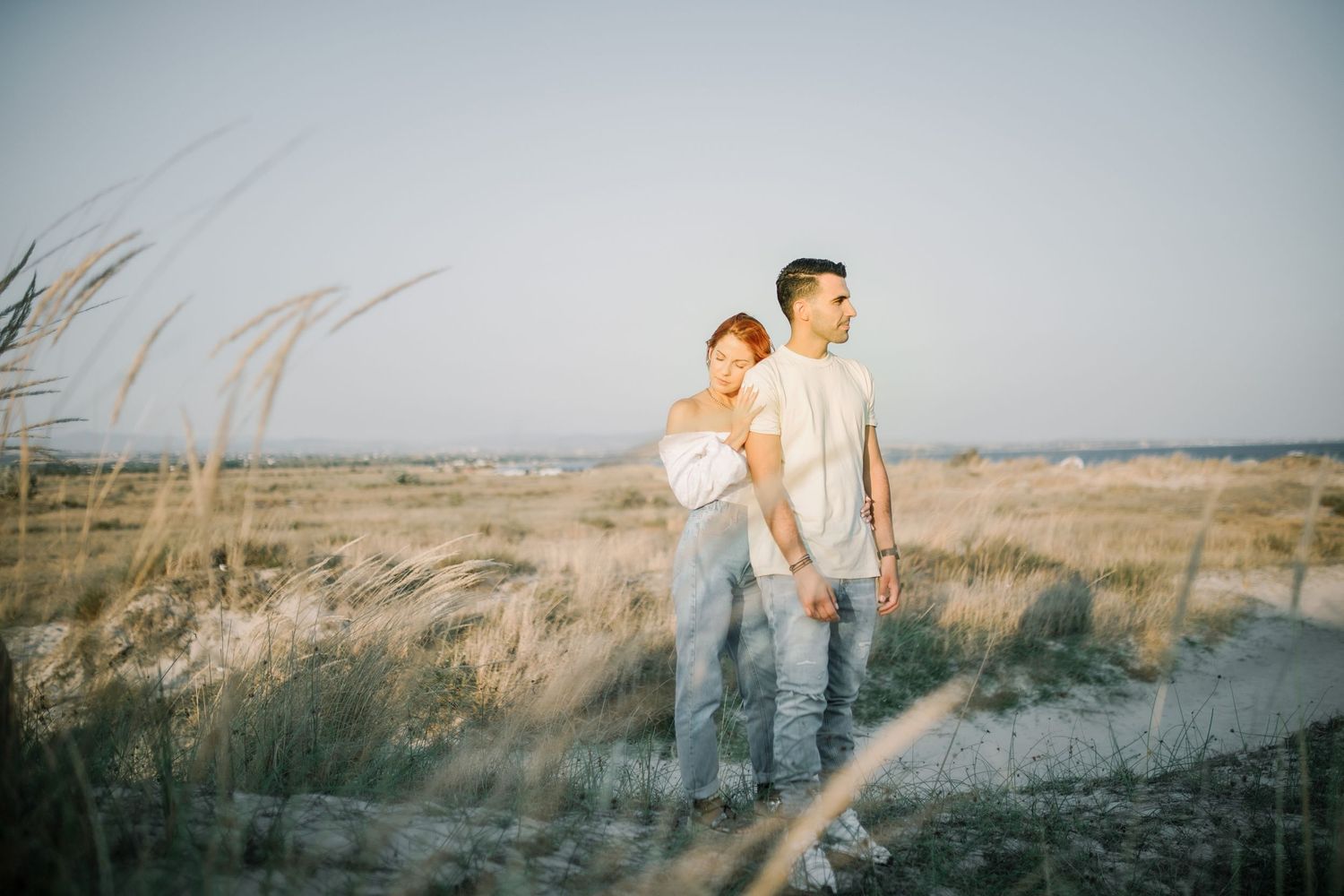 Two people walk hand in hand through tall grass in a field at sunset creating a romantic silhouette.