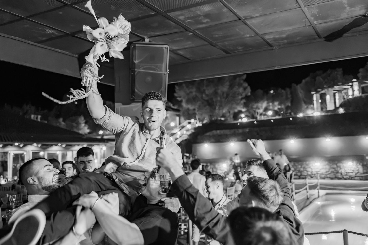 Man lifted on shoulders celebrating at night party with crowd cheering in black and white photo.