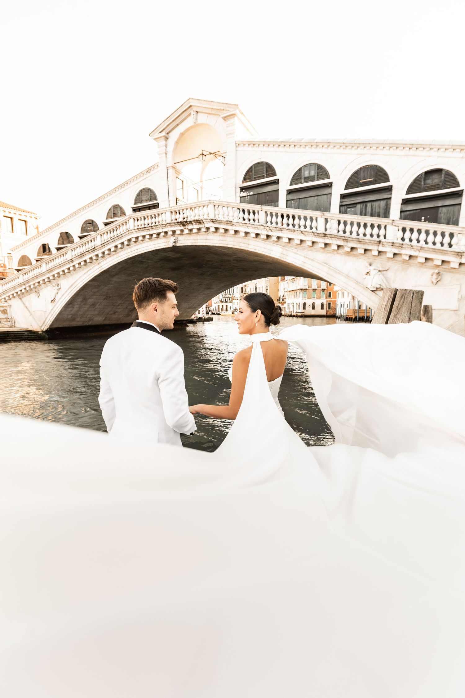 Romantic moment captured near the Rialto Bridge in Venice with flowing white fabric.