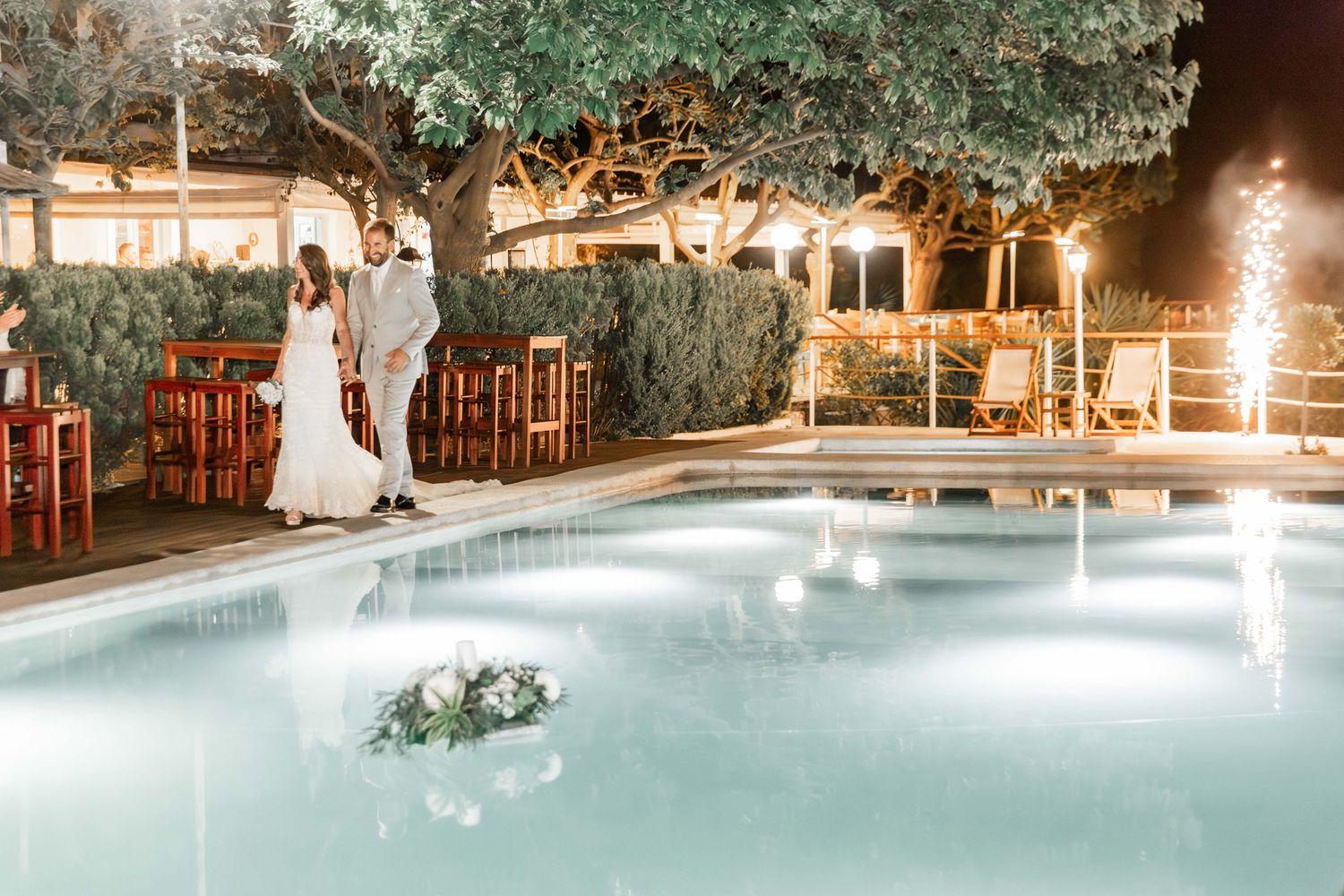 Elegant wedding celebration by an illuminated pool with string lights and outdoor decor.