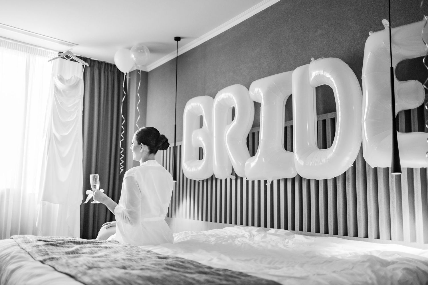 Black and white photo of a wedding preparation room with large BRIDE text on the wall.