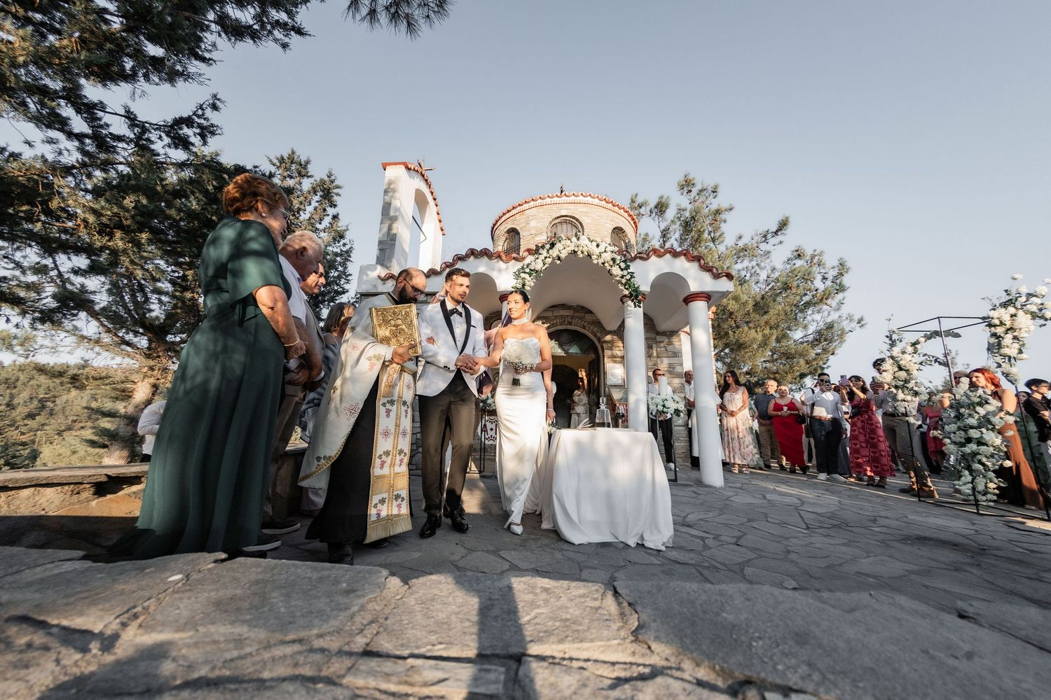 Scenic mountain wedding ceremony with guests gathered on rocky overlook at sunset.