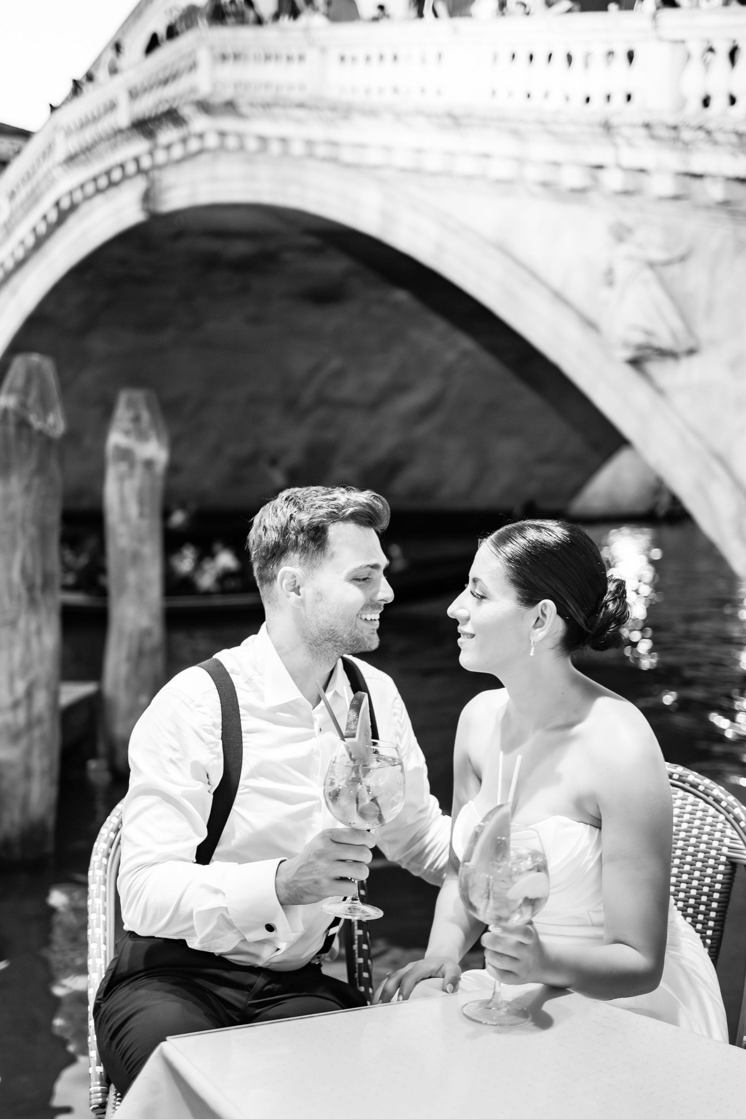 Couple sharing drinks and laughter at an outdoor cafe under elegant stone arches in Venice.