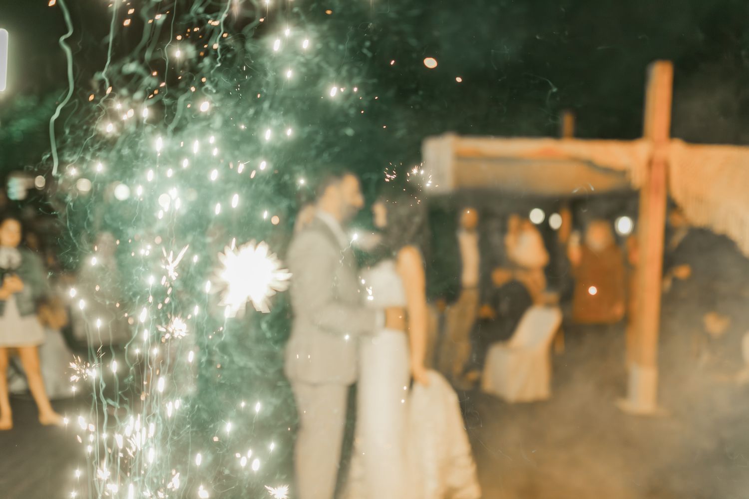 Sparklers create a magical atmosphere during an outdoor evening wedding celebration.