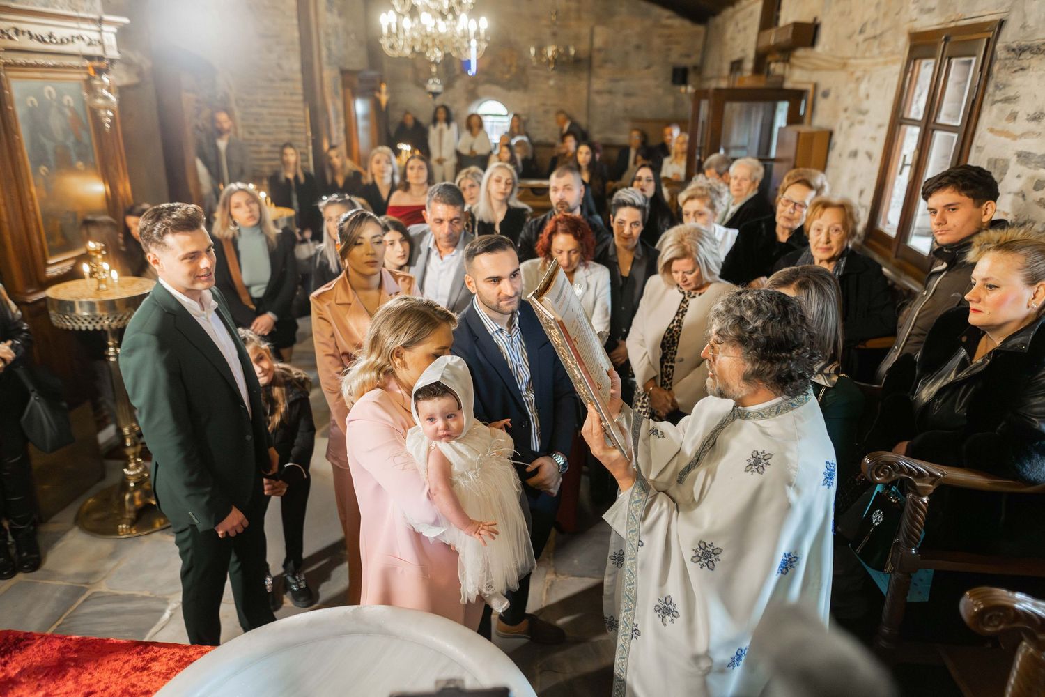 Wedding guests dance and celebrate together on a wooden dance floor under warm lighting at an indoor reception venue.