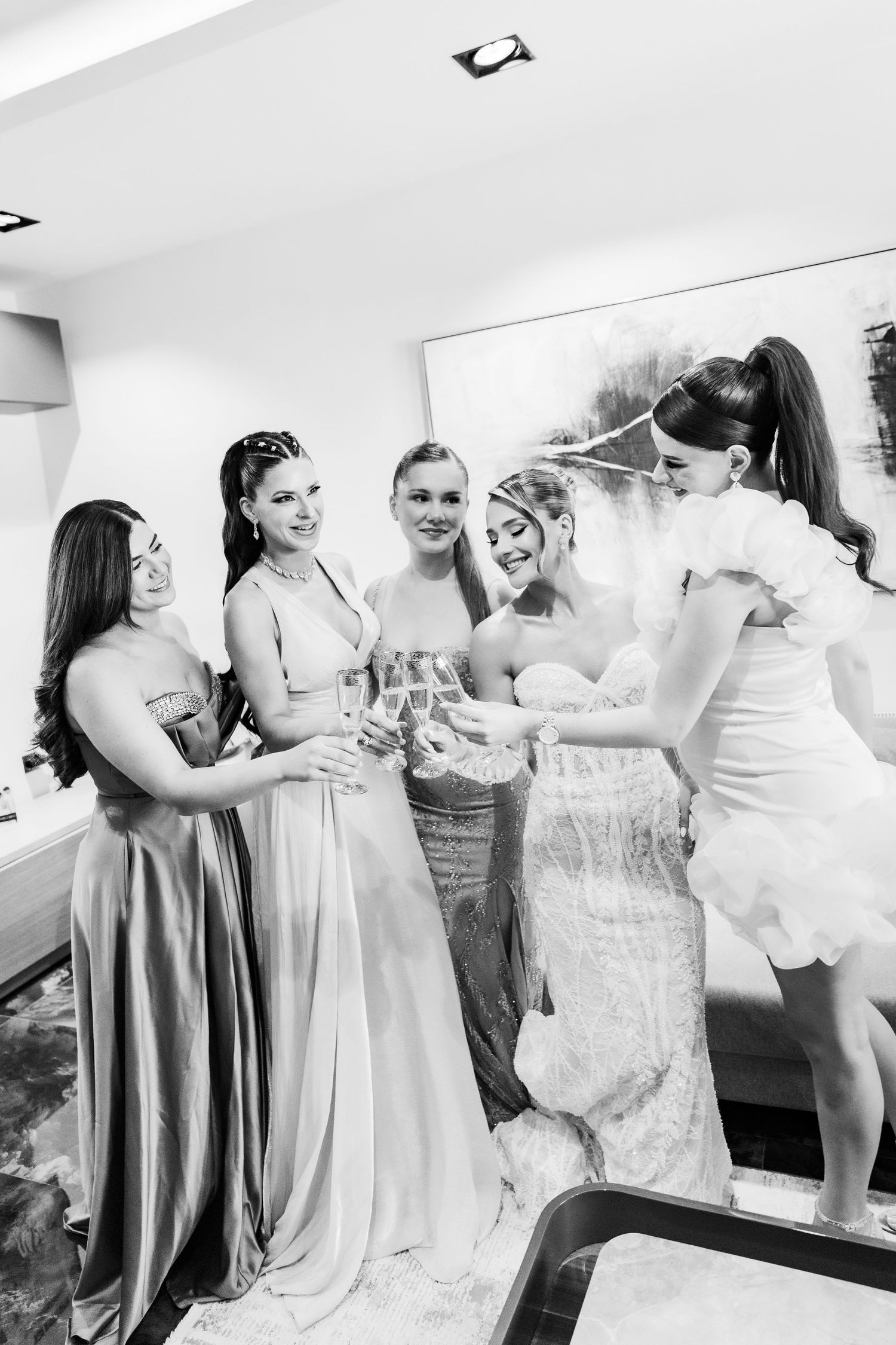 Bride and bridesmaids celebrating together in elegant gowns, sharing a joyful moment during wedding preparations.