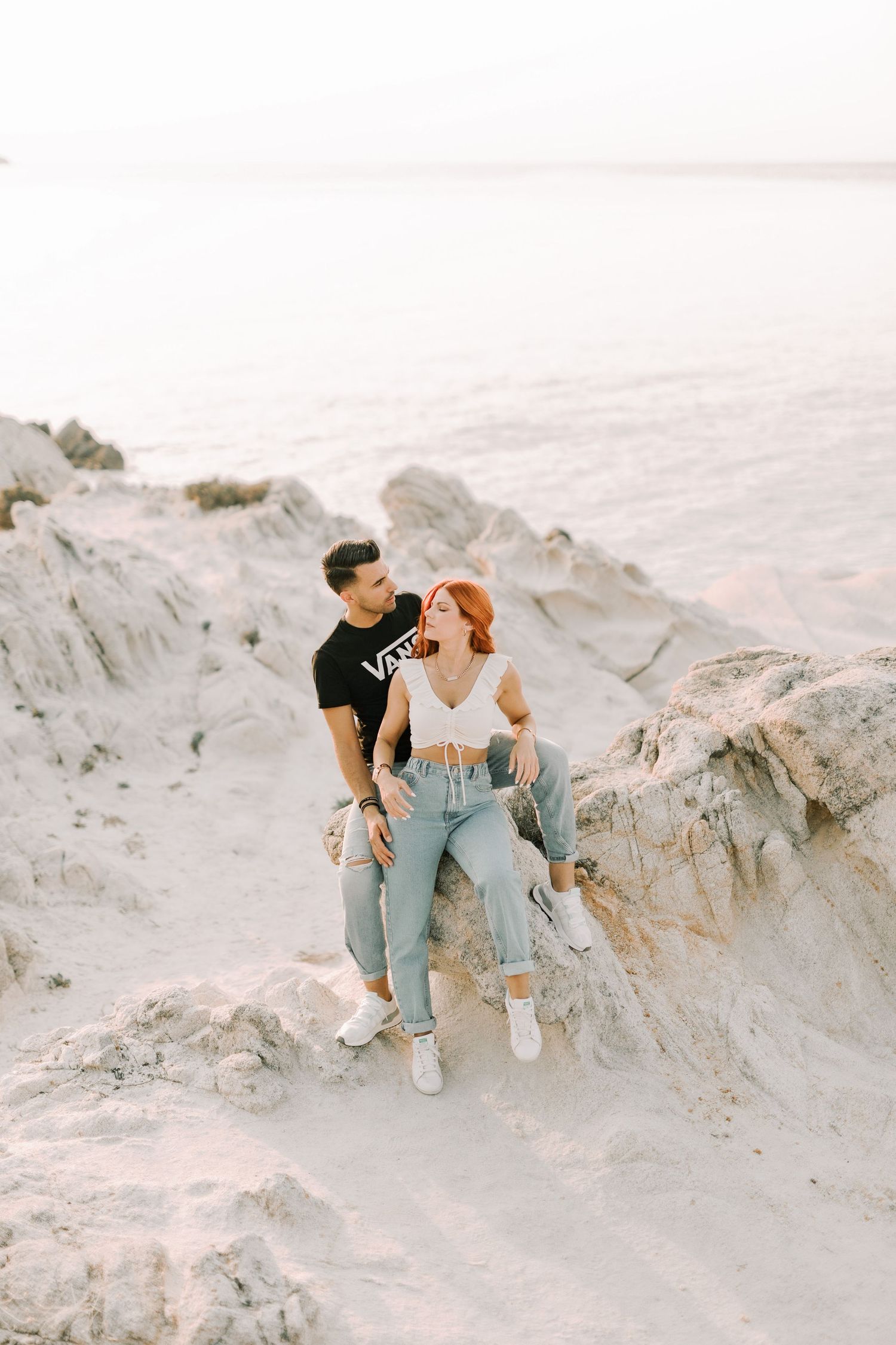 A couple sits together on white sandy cliffs during a romantic outdoor photoshoot at sunset.