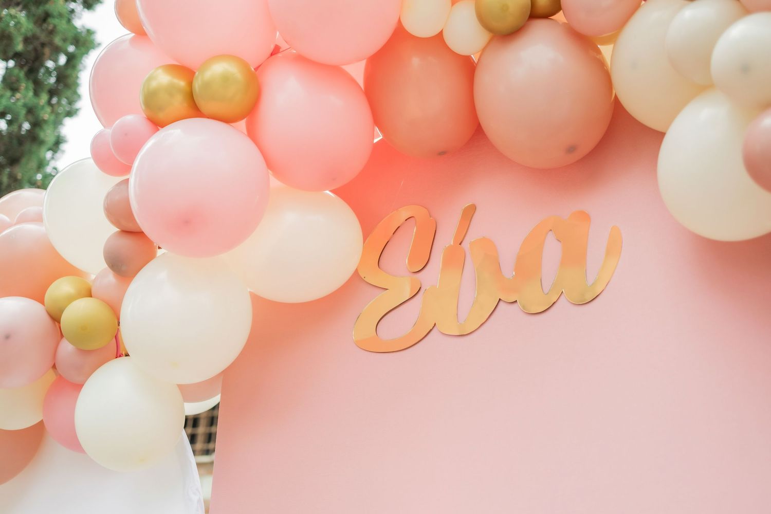 A festive balloon garland arch in coral pink, white and gold colors creates an elegant party decoration display.