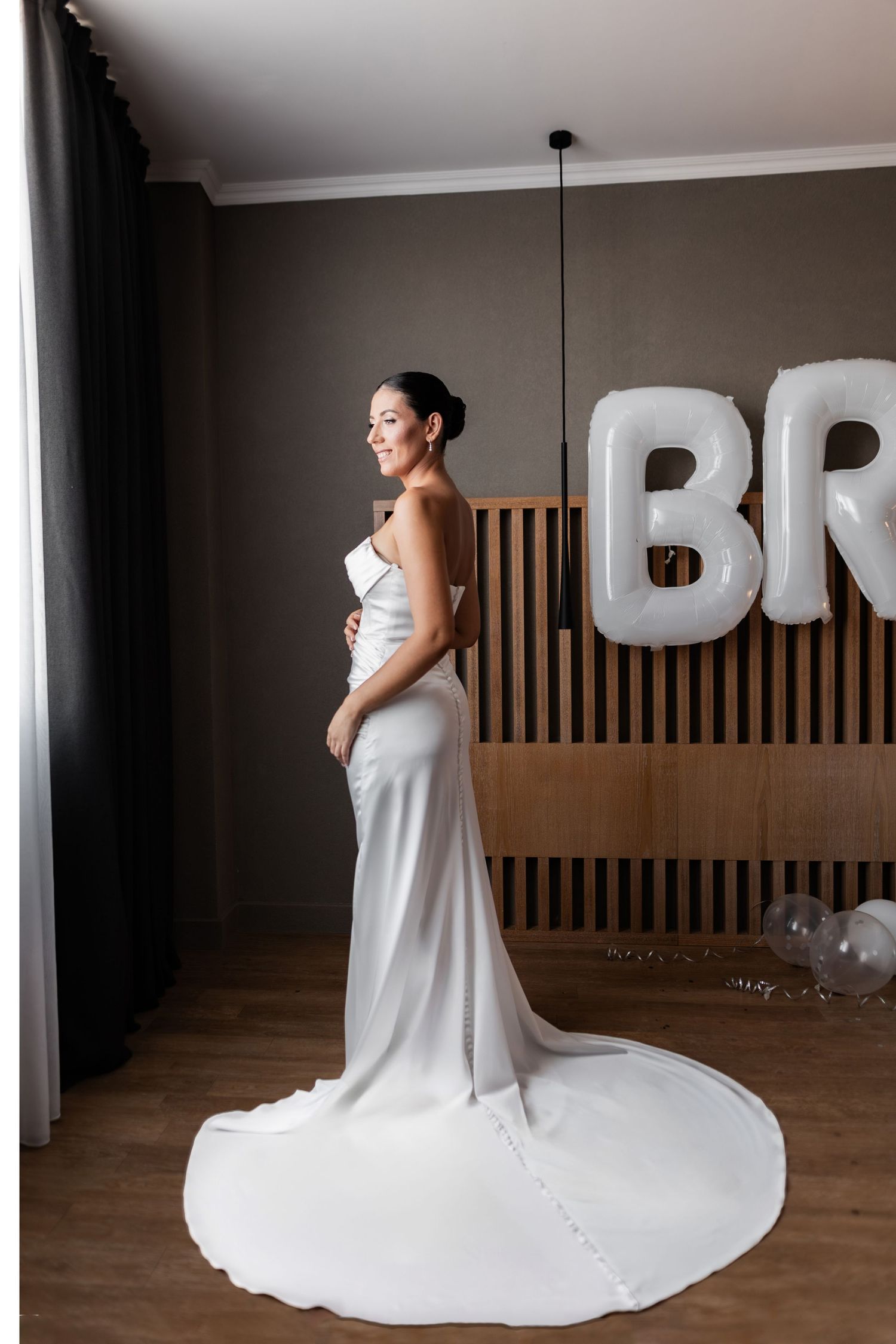 Full-length shot of flowing white wedding dress with train against wooden wall decor.
