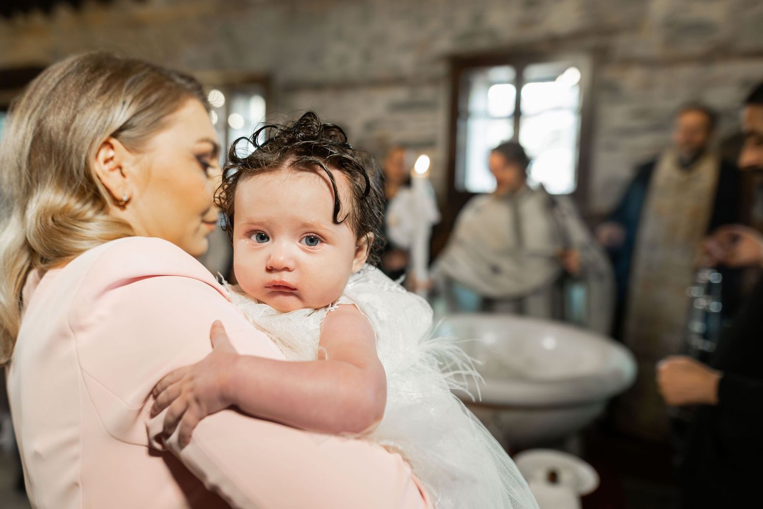 A baby in white attire is held during what appears to be a baptism ceremony in a church setting.