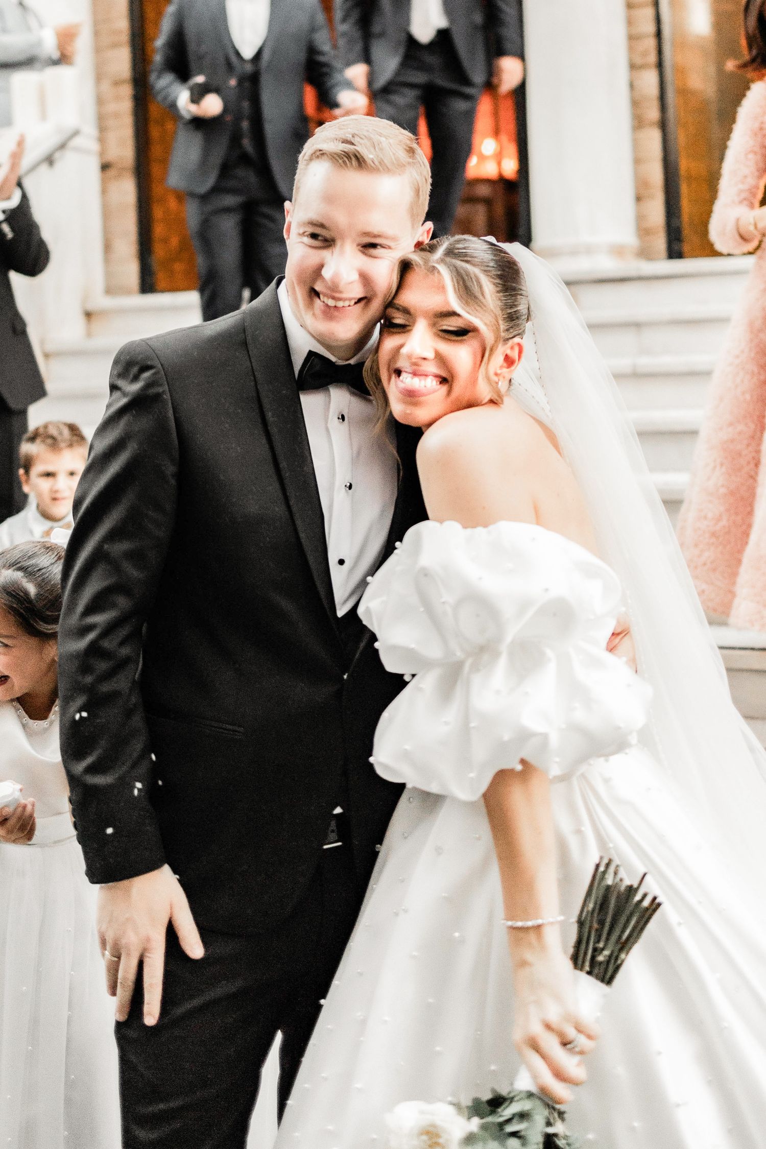 Joyful wedding celebration with guests throwing confetti outside an elegant venue.