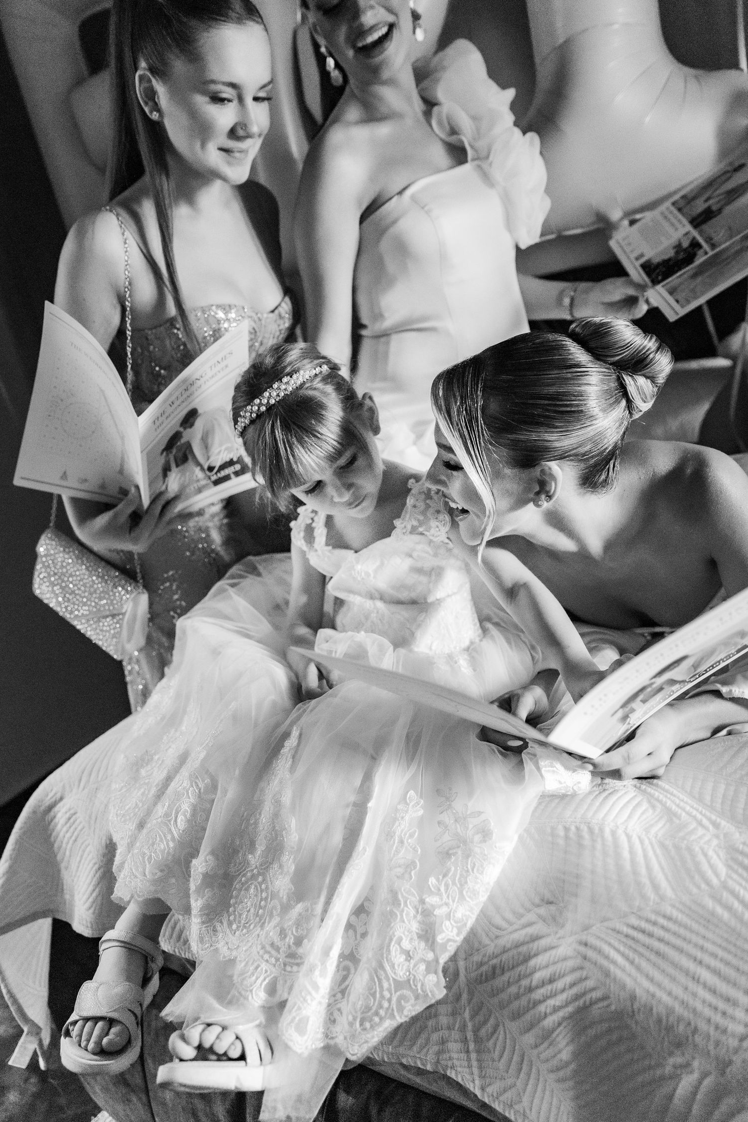 Black and white photo of bridesmaids and flower girl reading together before a wedding ceremony.