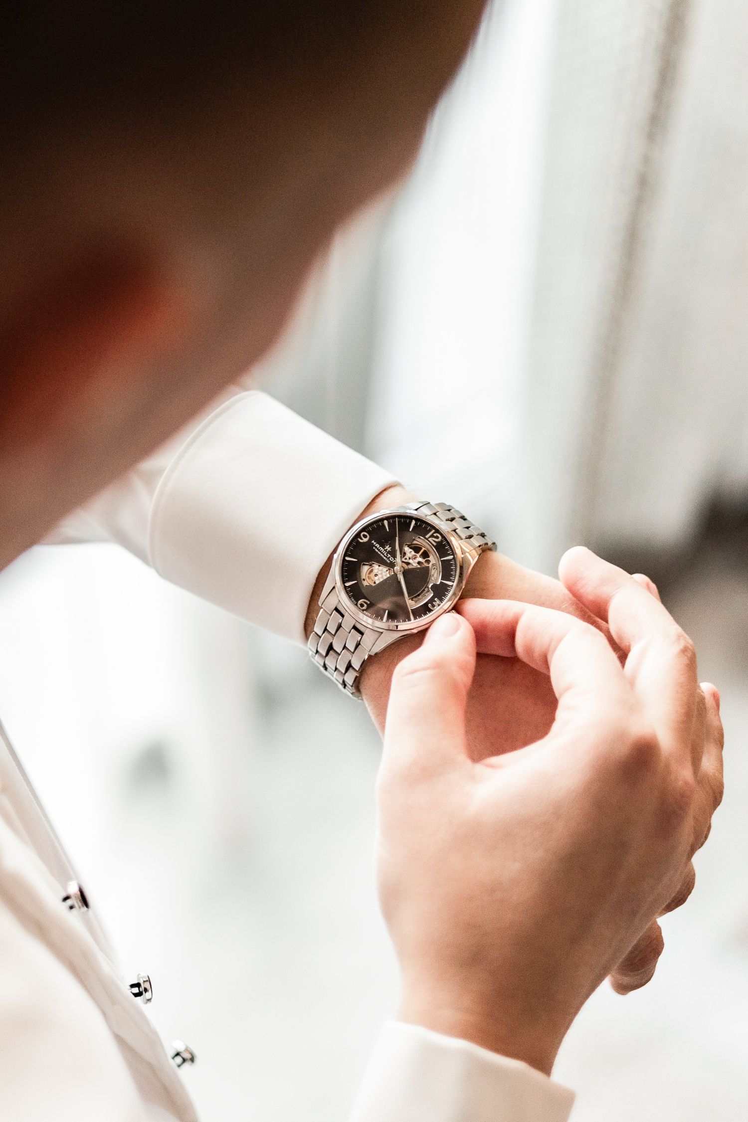 Hands holding and examining a detailed wedding ring against a bright white background.