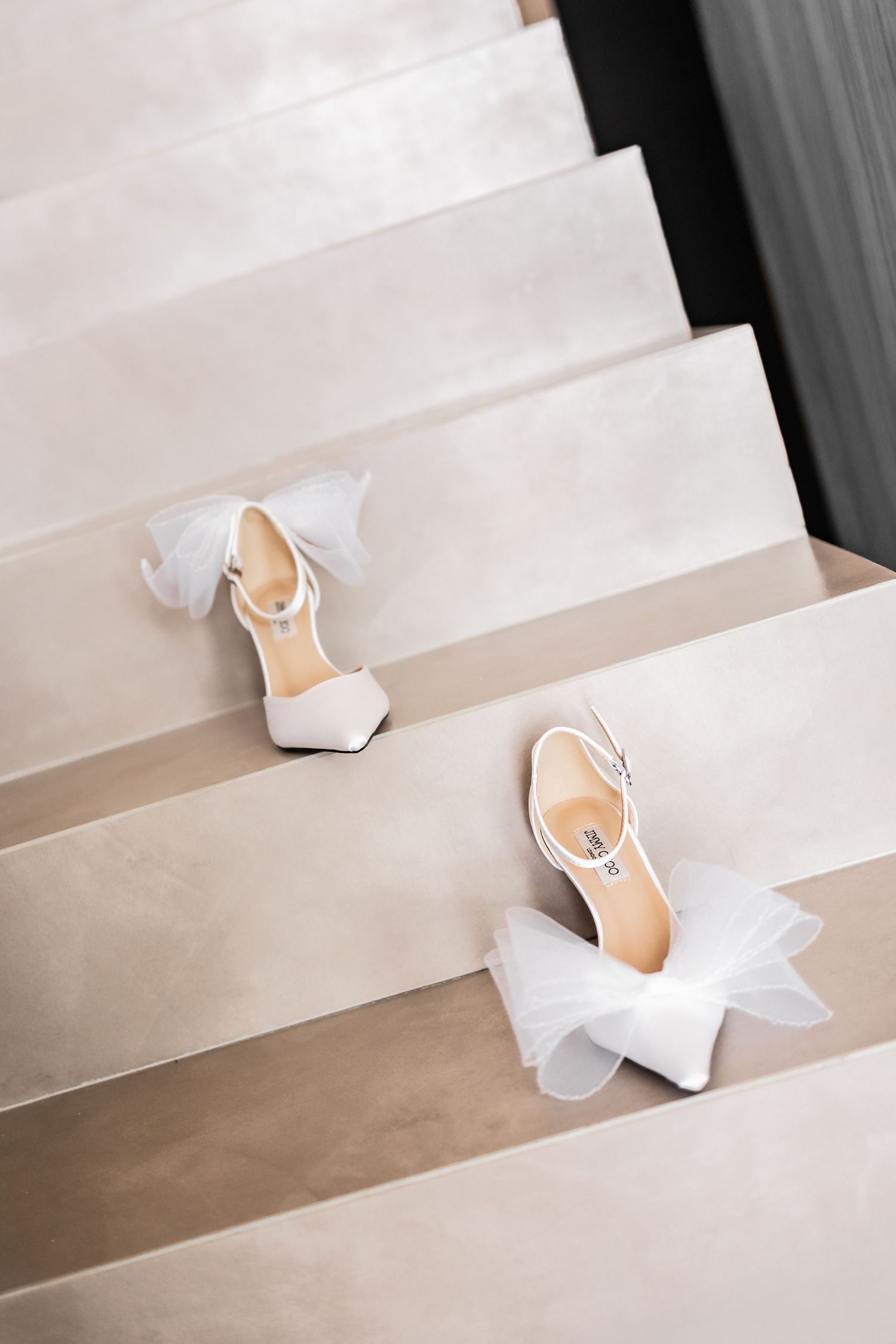 Elegant white bridal shoes placed on concrete steps with soft lighting.