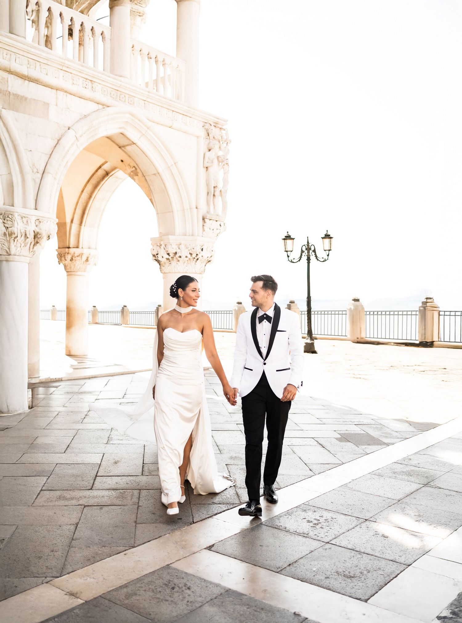 A couple walking hand in hand under the ornate arches of Venice's Doge's Palace.