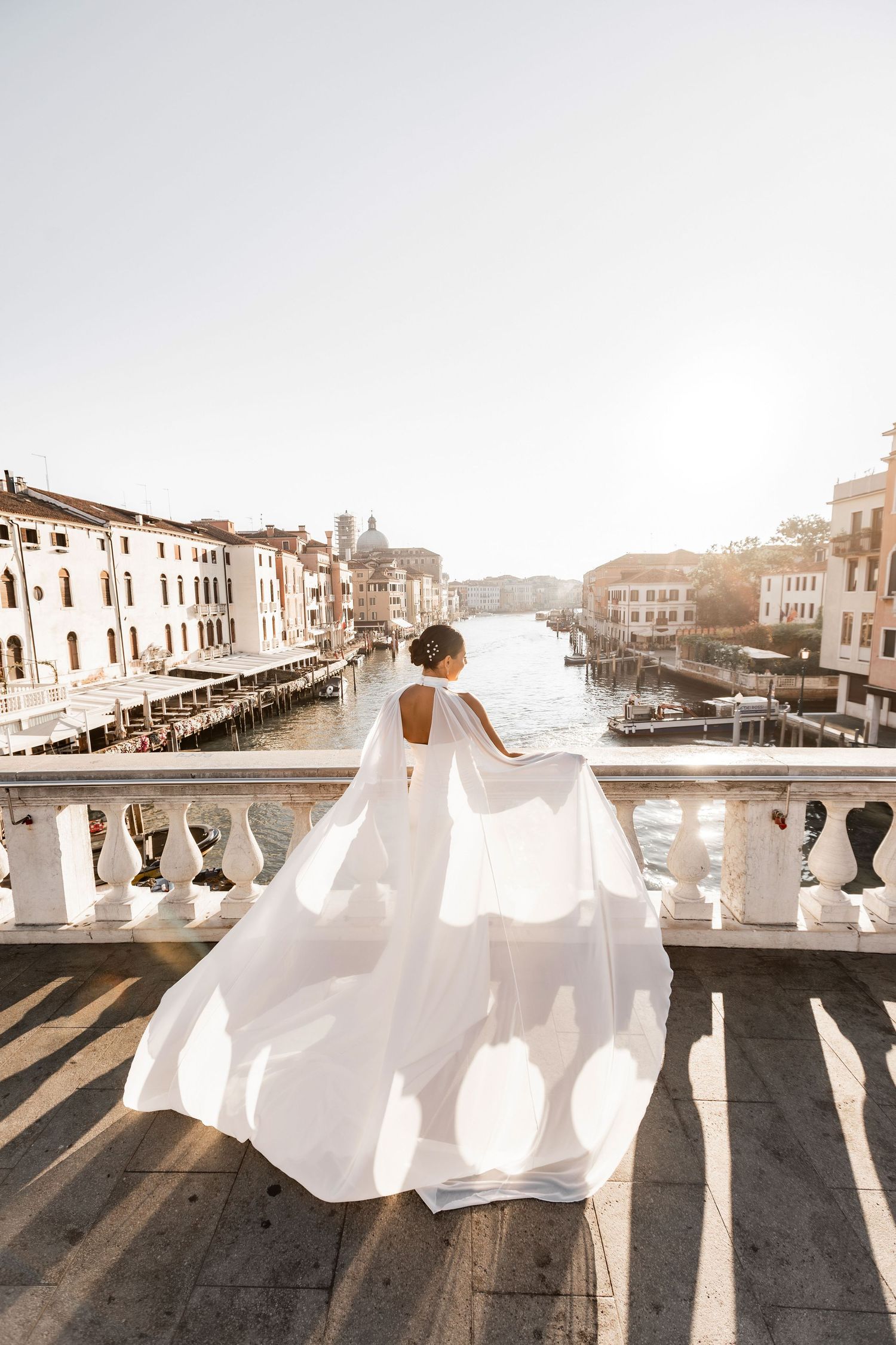 A flowing white dress creates dramatic shadows against a stone balustrade in Venice at sunset.