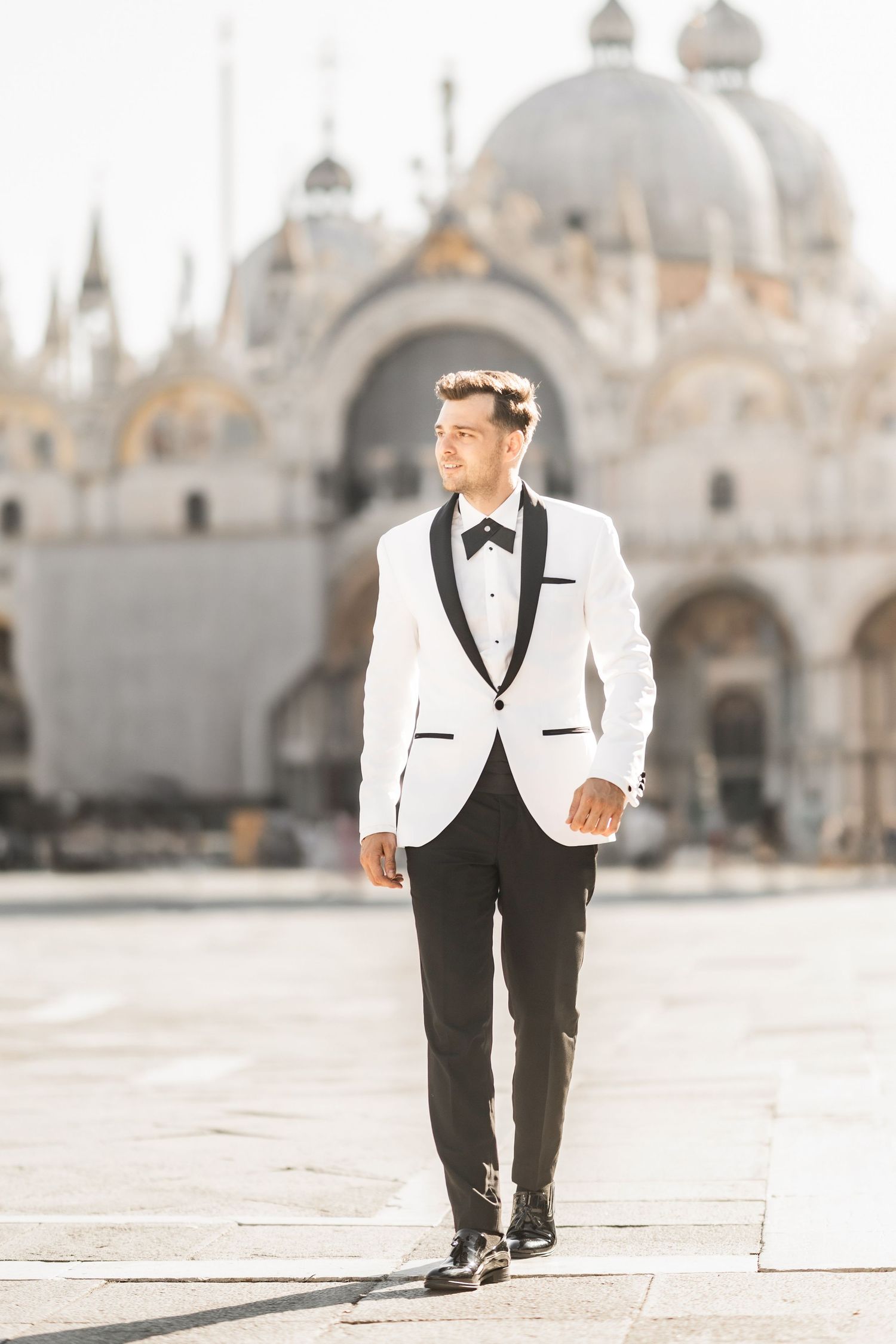 Elegant groom in white tuxedo walking across St. Mark's Square in Venice.