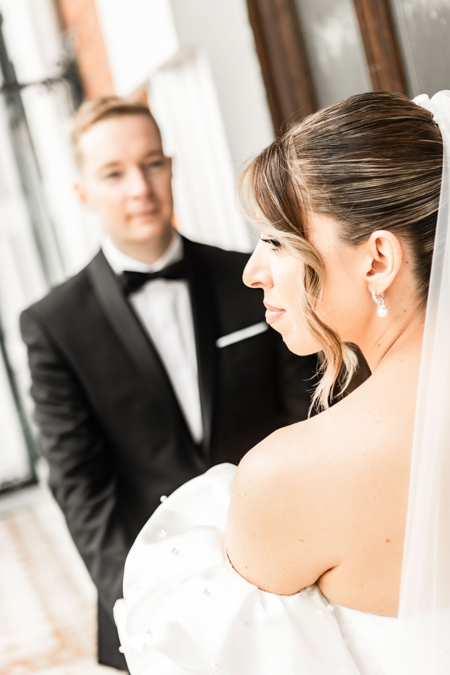 A romantic wedding moment captured in soft light with the bride in white and groom in classic black tuxedo.