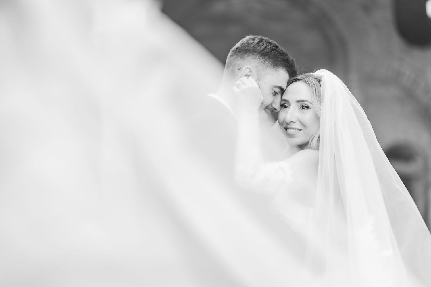 Black and white wedding photo of smiling bride in veil embracing groom, romantic couple portrait.