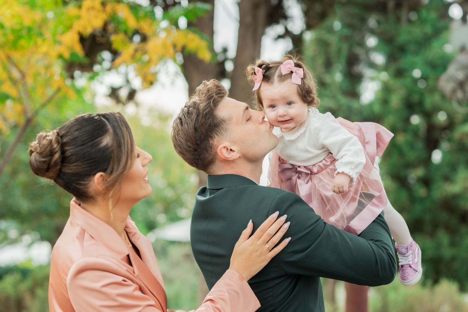 A family shares a tender moment together outdoors in a garden setting with green foliage in the background.