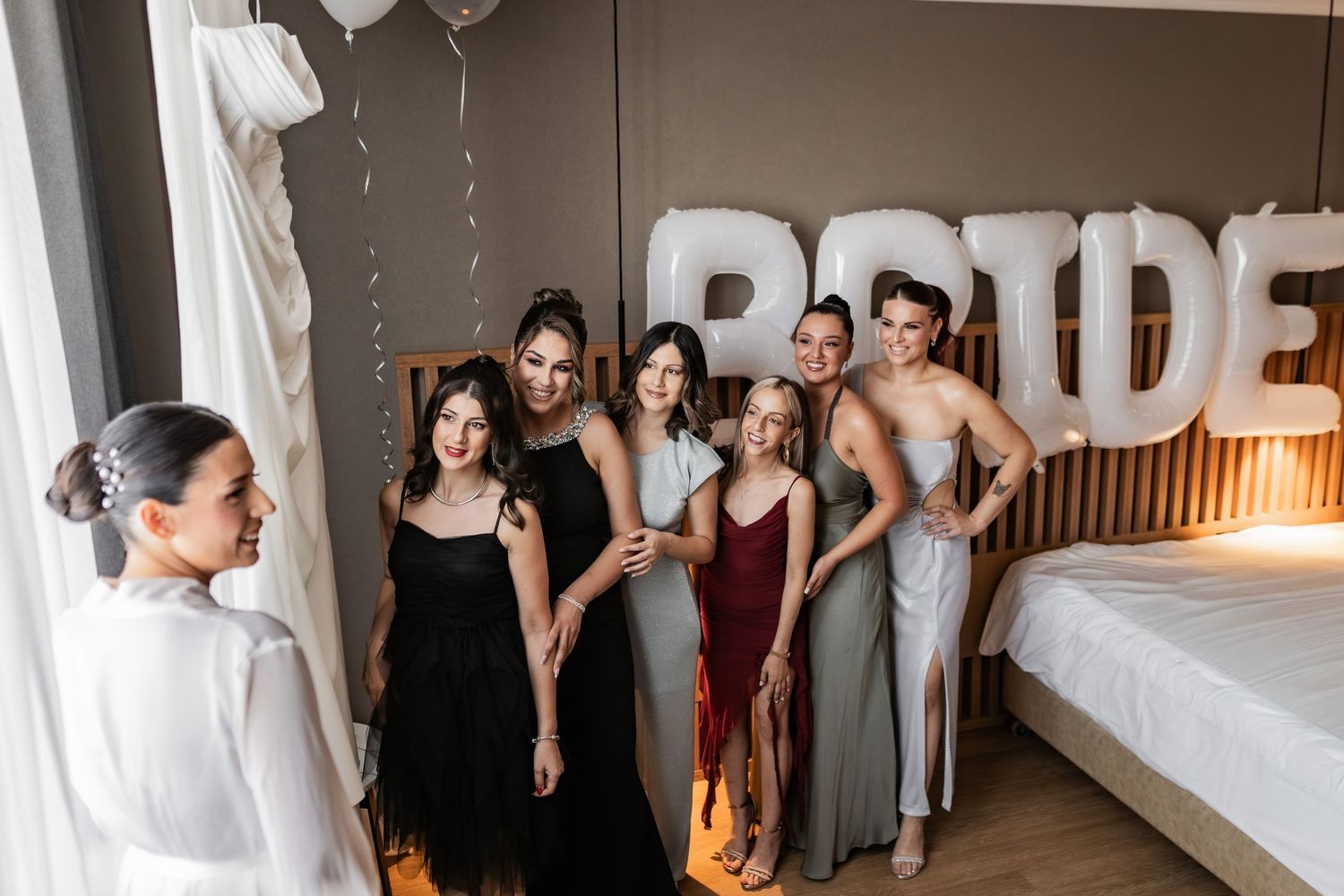 Wedding party gathers in hotel room with BRIDE backdrop and festive decorations.
