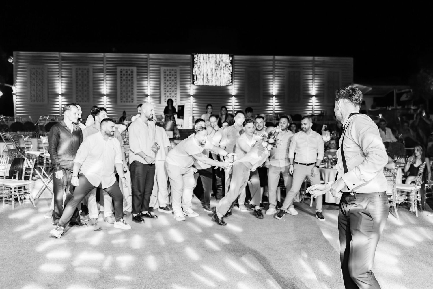 Black and white photo of wedding guests dancing in formation at a reception.