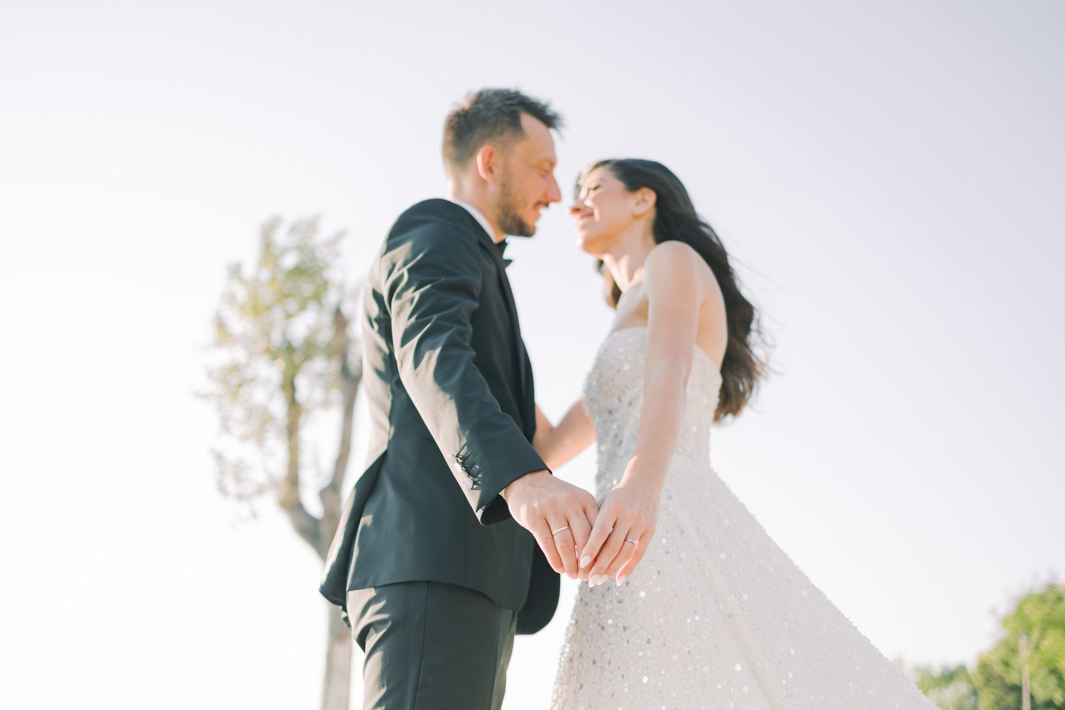 Newlywed couple shares a romantic kiss in an outdoor garden setting wearing elegant wedding attire.