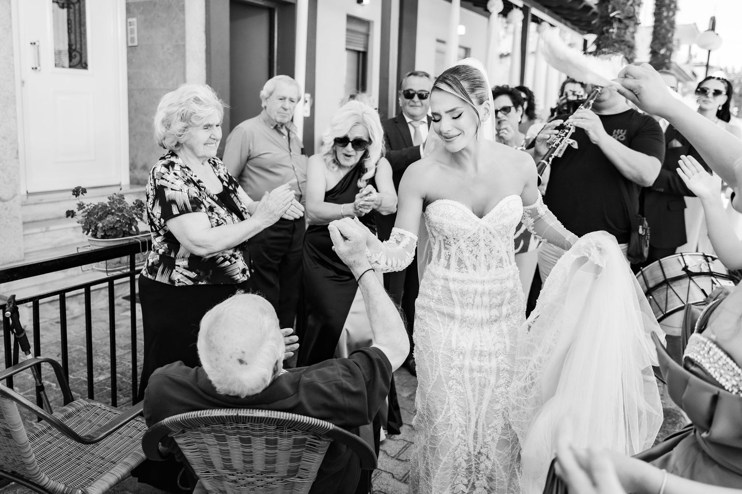 Black and white photo of a bride in a lace gown surrounded by guests at an outdoor wedding celebration.