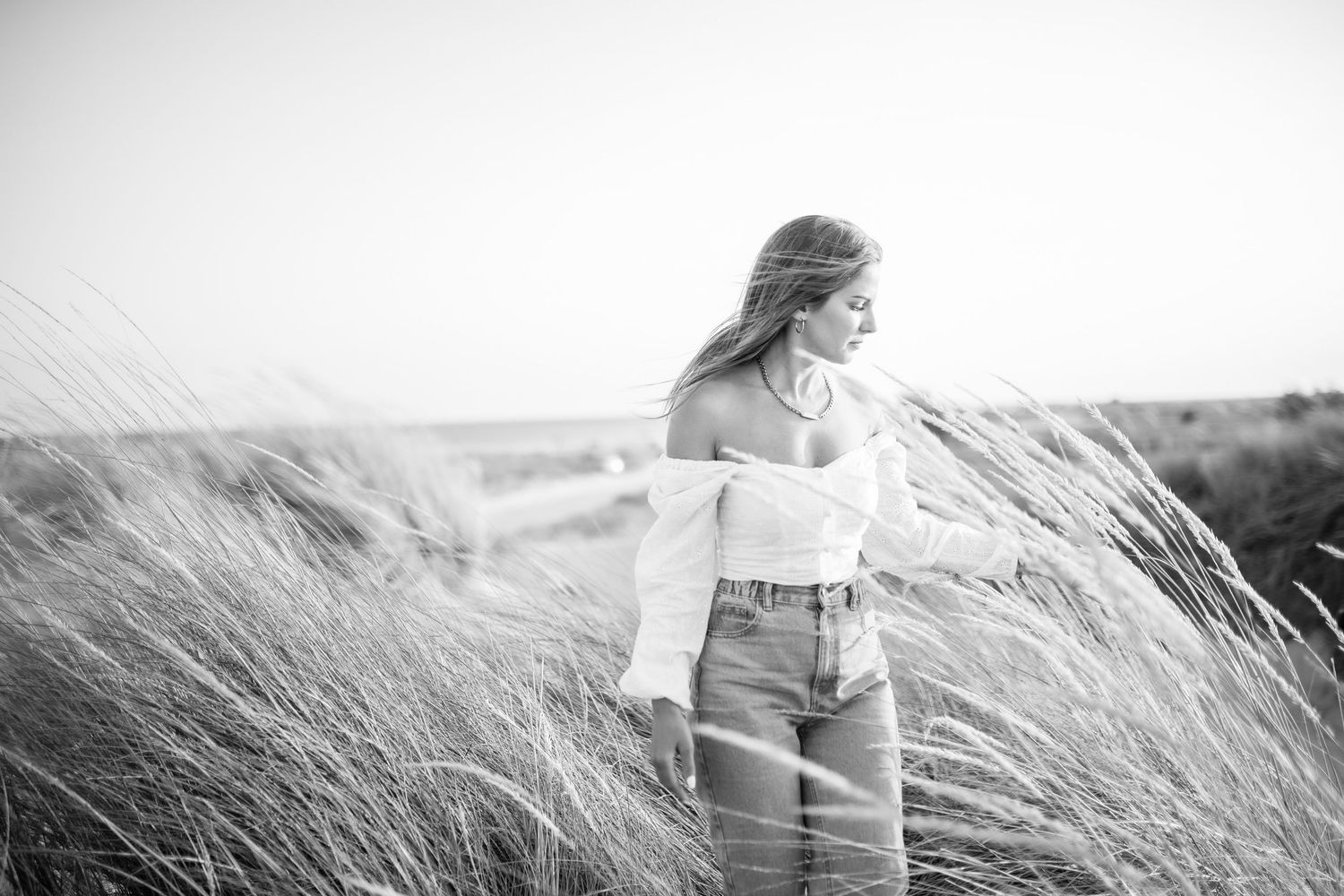 A series of black and white photographs showing a person sitting in tall grass on a windy day by the ocean.