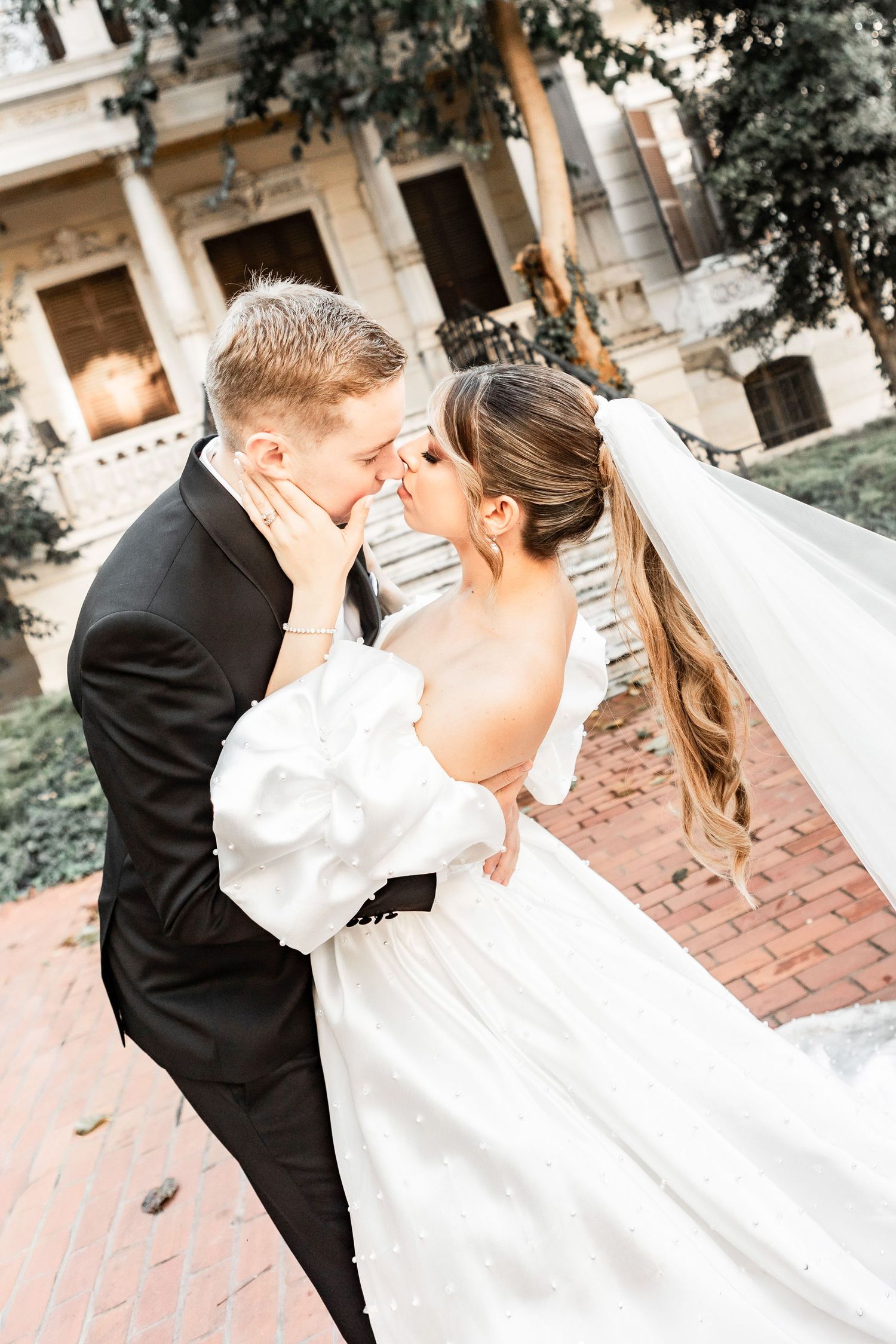 Passionate wedding kiss captured in front of historic building steps.