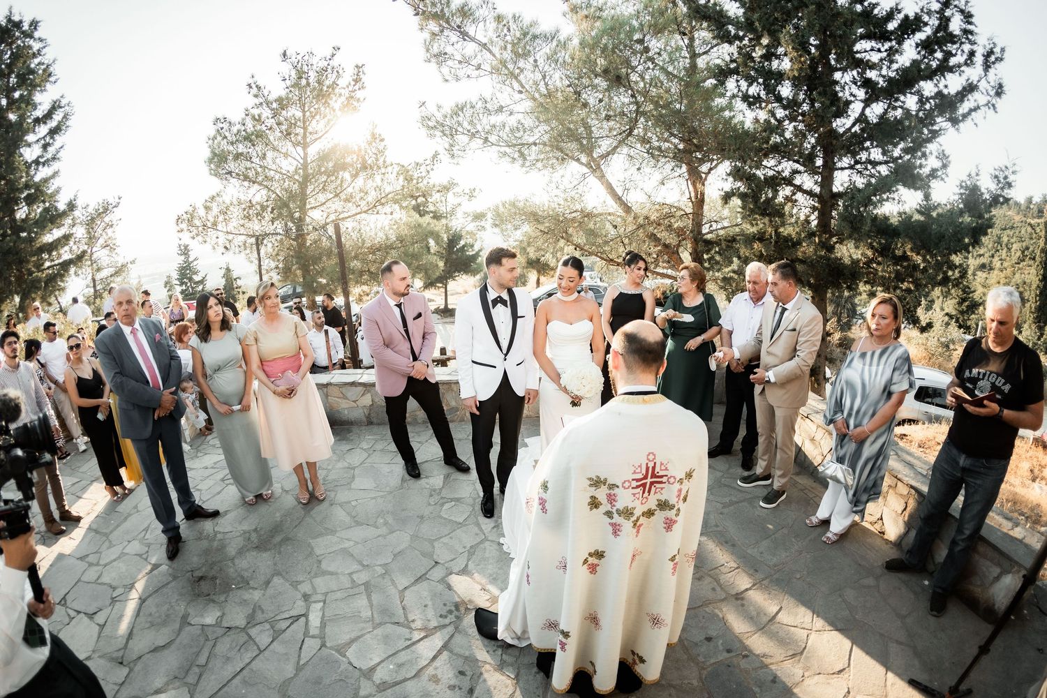 Panoramic view of an outdoor wedding ceremony with guests gathered among pine trees.