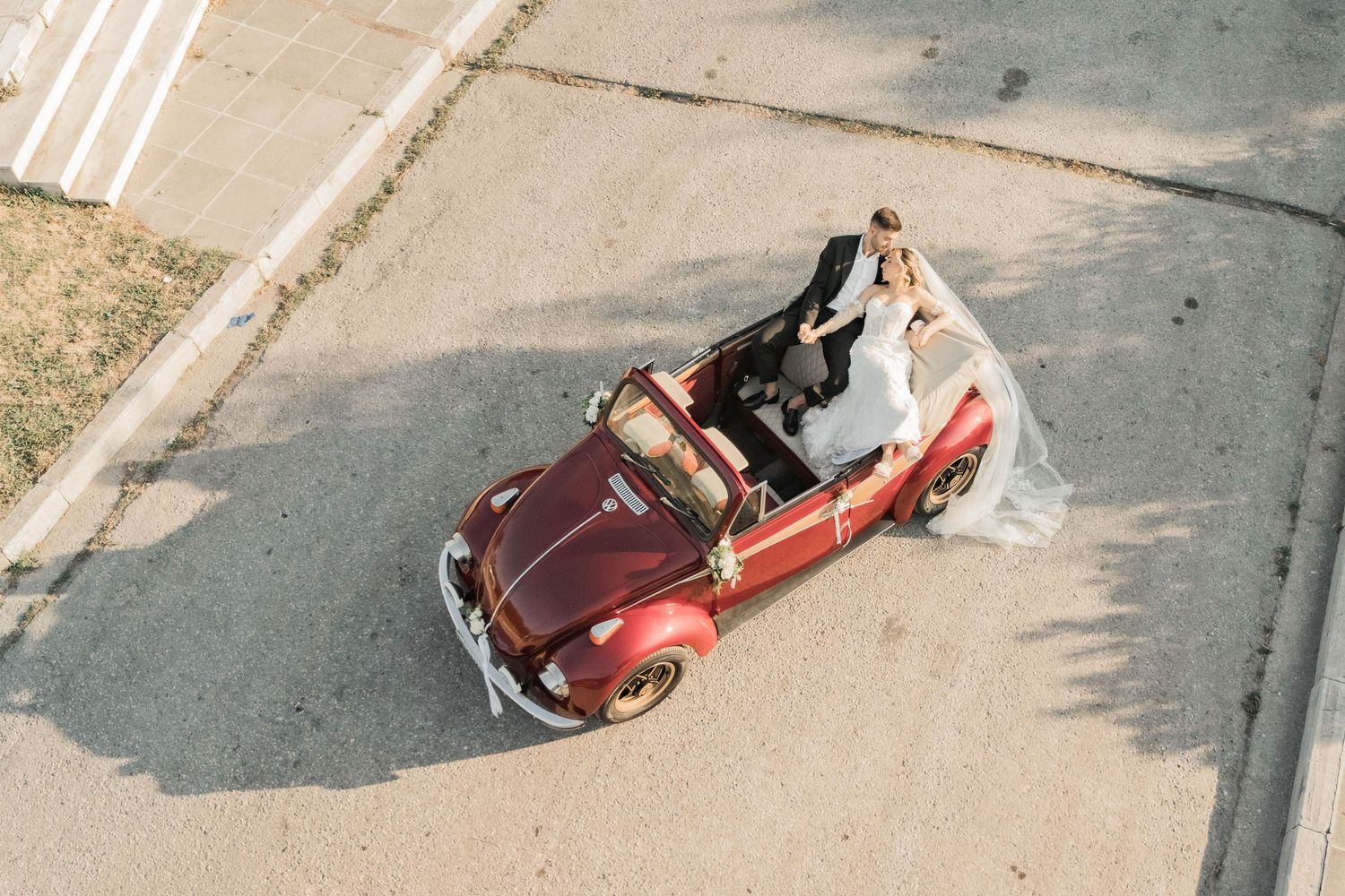 Aerial view of a bride and groom kissing in a vintage red convertible VW Beetle on their wedding day.