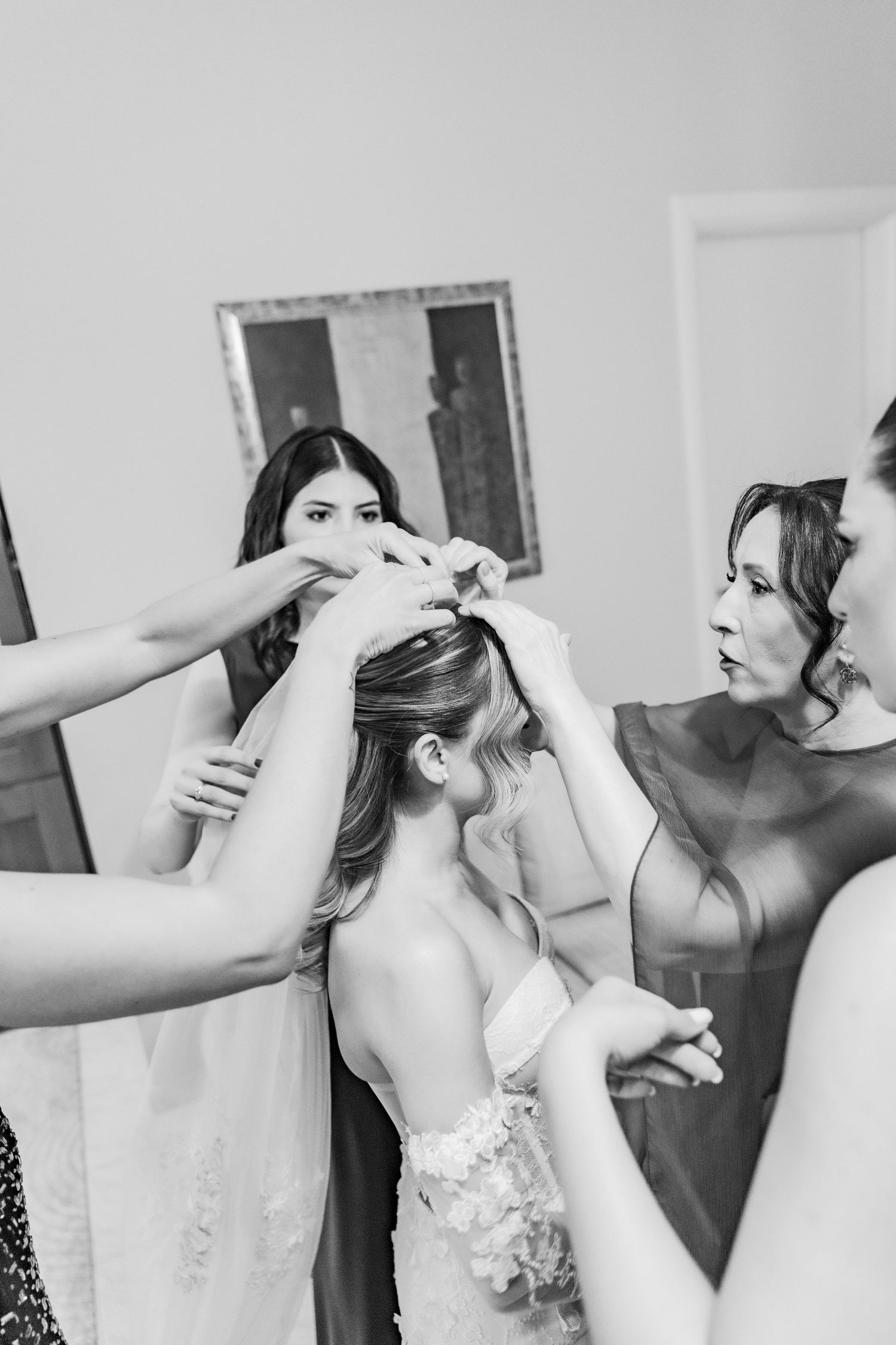 Bridesmaids helping bride with veil in black and white wedding preparation photo.