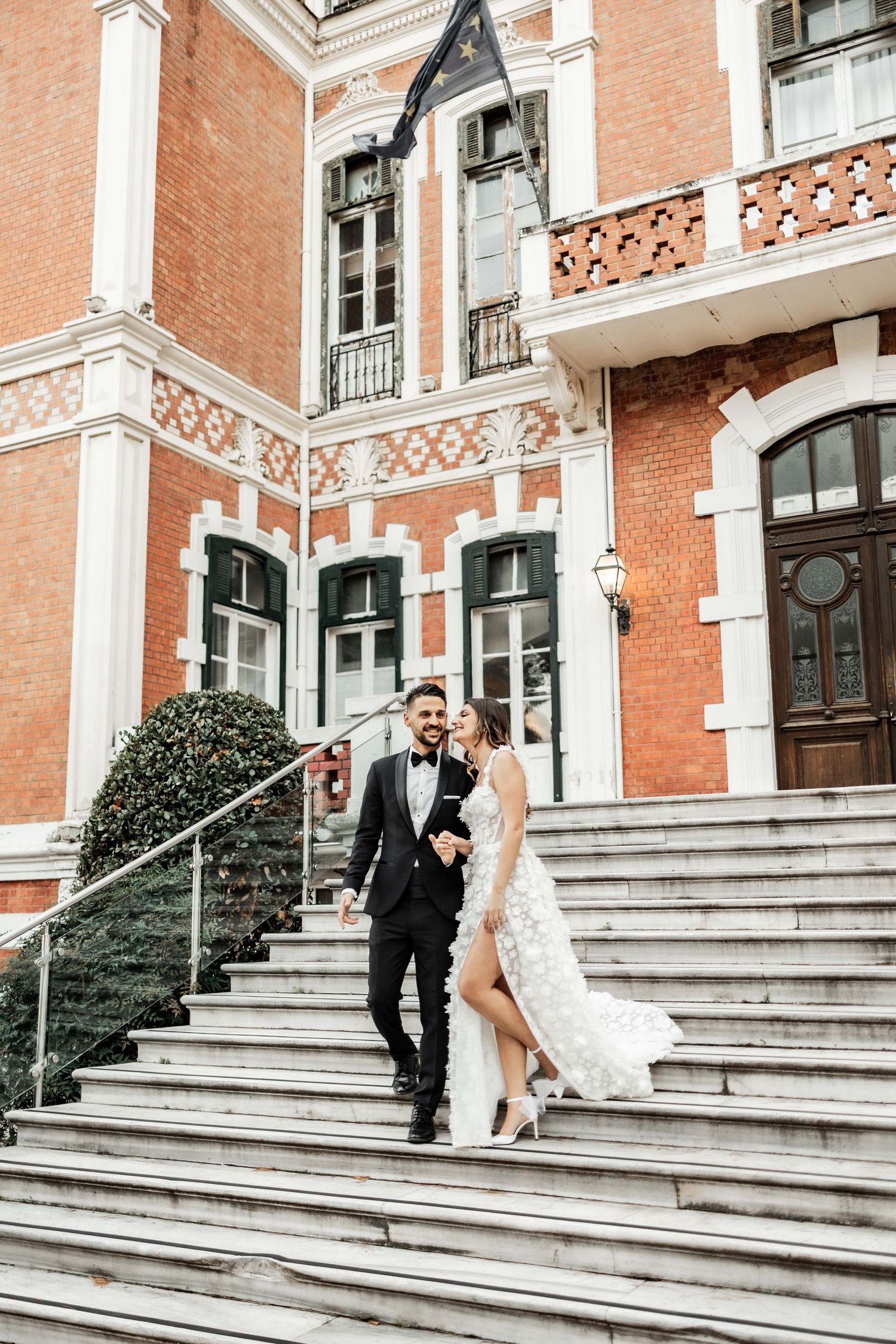 A stylish wedding couple descending stone steps of a historic brick building with ornate details.