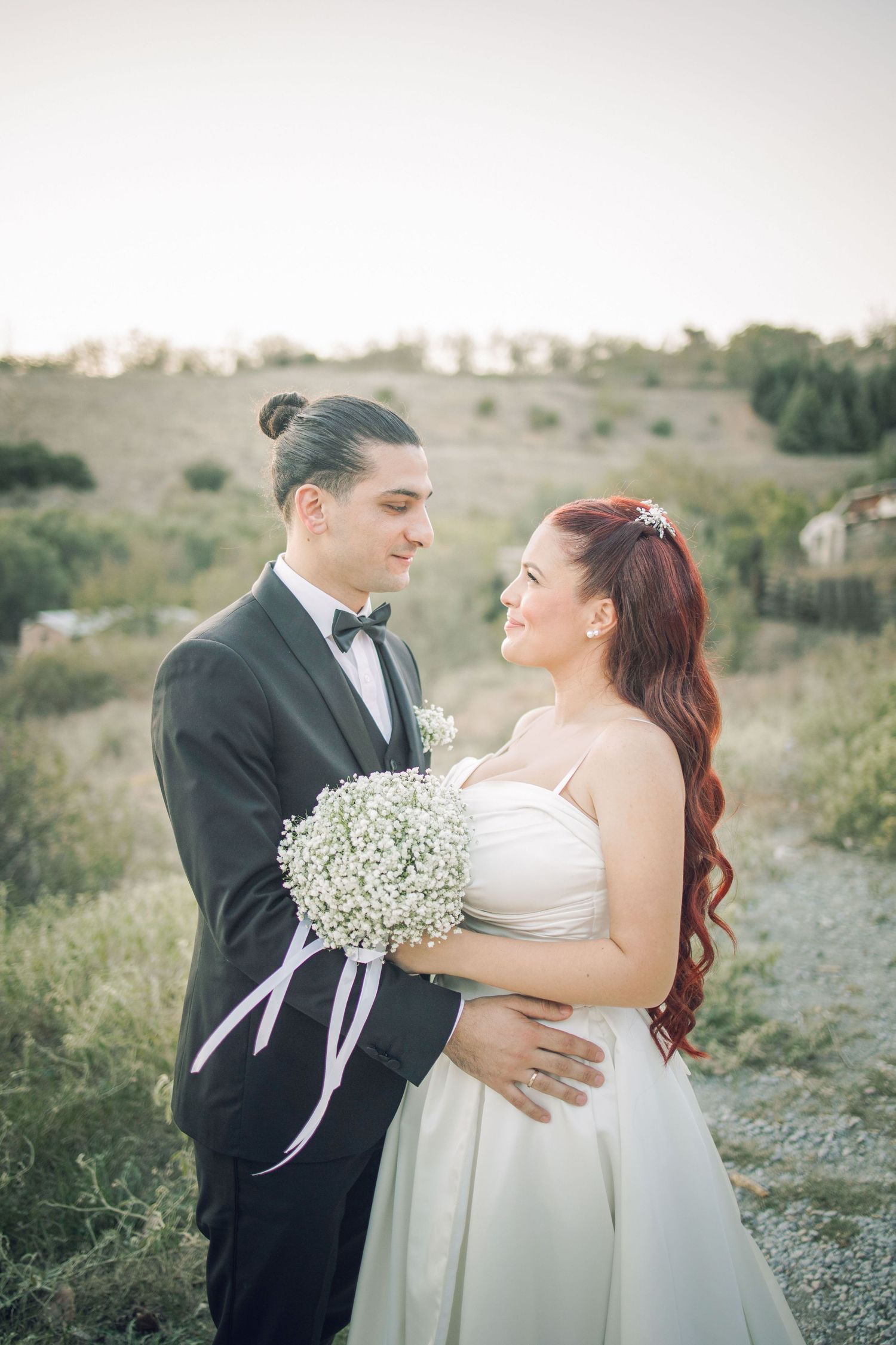 Romantic wedding couple embraces outdoors in a natural setting with delicate baby's breath flowers and formal attire.