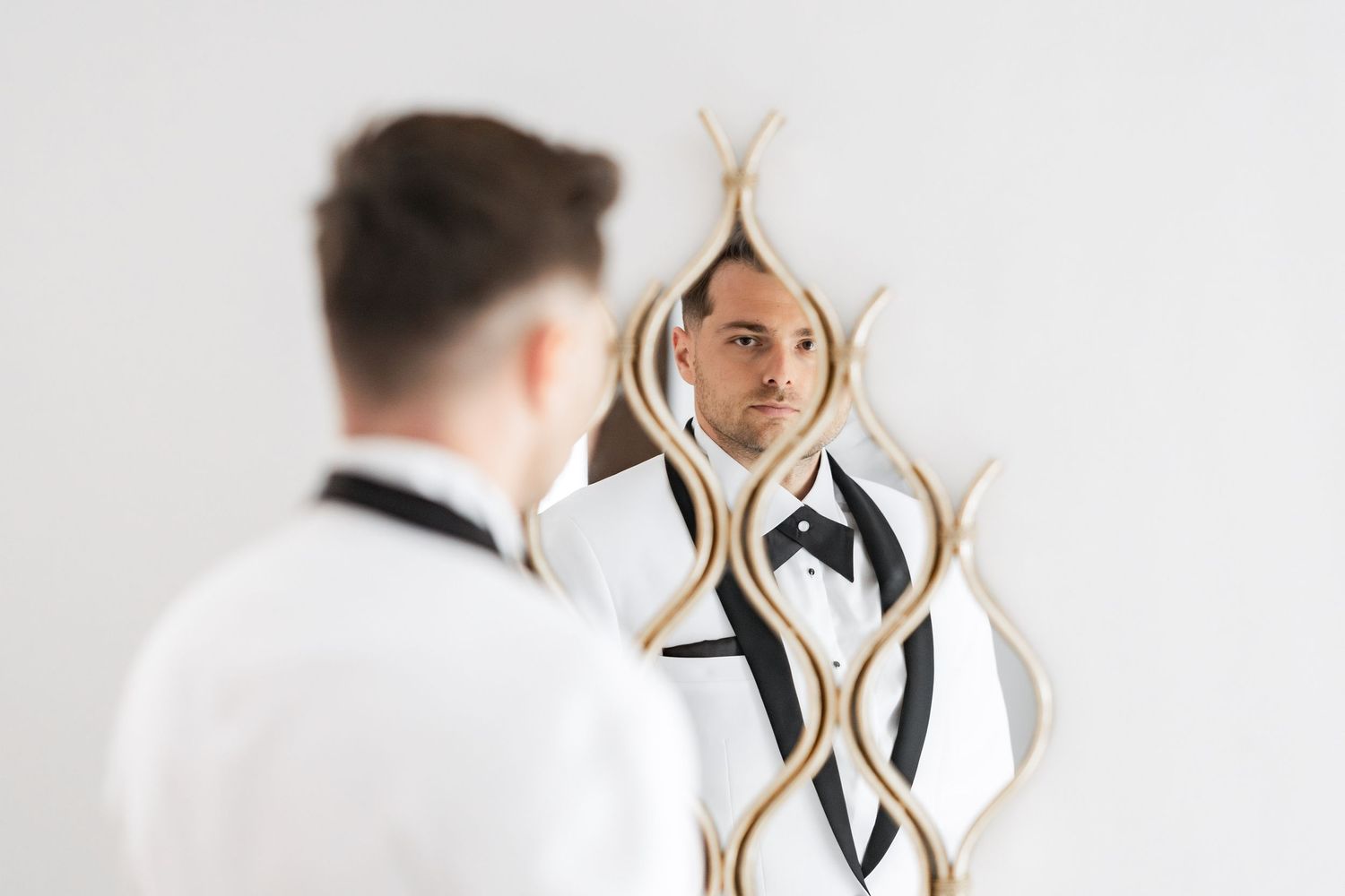 Artistic mirror reflections showing formal attire preparation in bright white space.