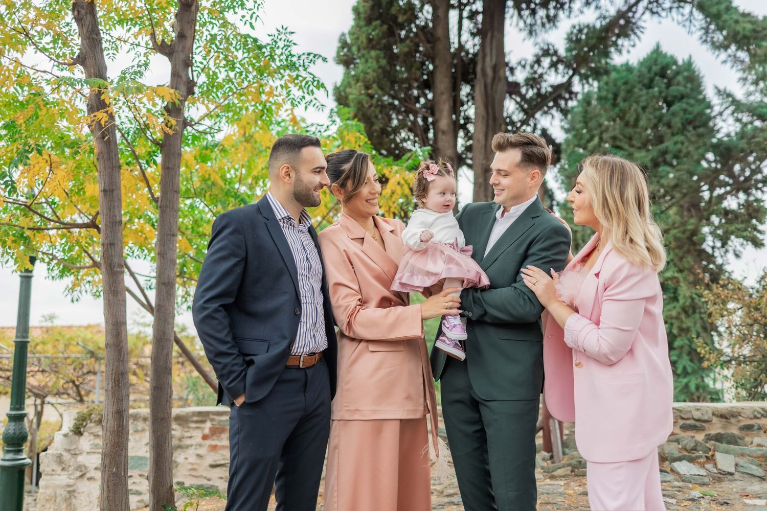 A group celebrates outdoors in formal attire during a fall day with colorful autumn trees in the background.