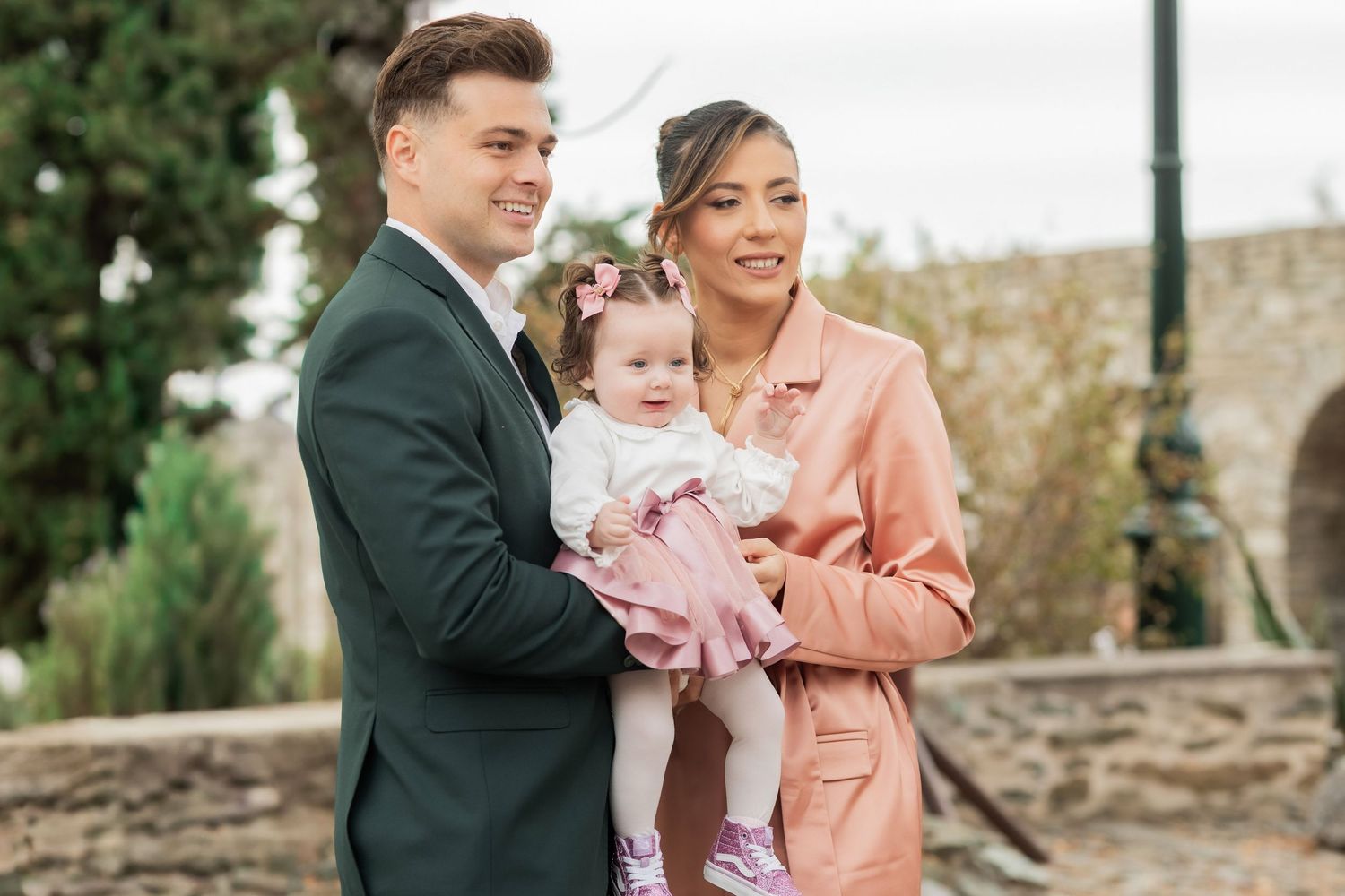 A couple shares joyful moments with their baby during an outdoor family photo session in a garden setting.