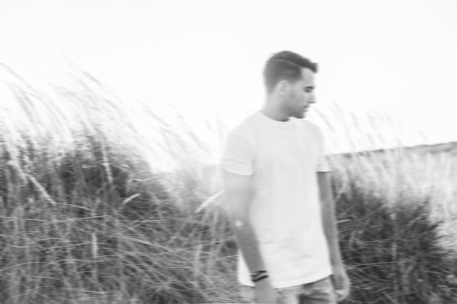 A series of black and white photographs showing a person walking through tall grass and reeds in a natural setting.