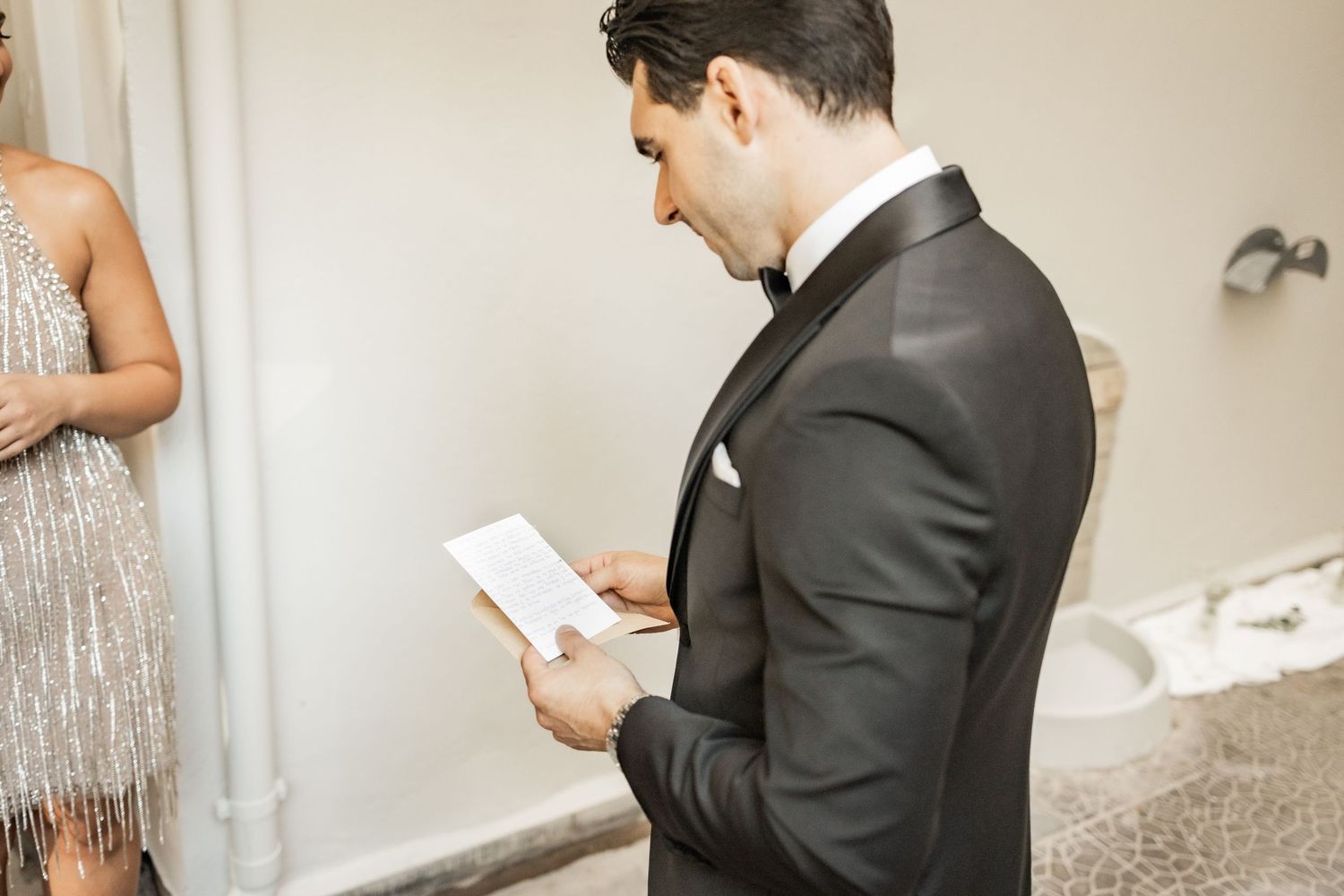 Groom in black tuxedo reading vows from a card during wedding ceremony.