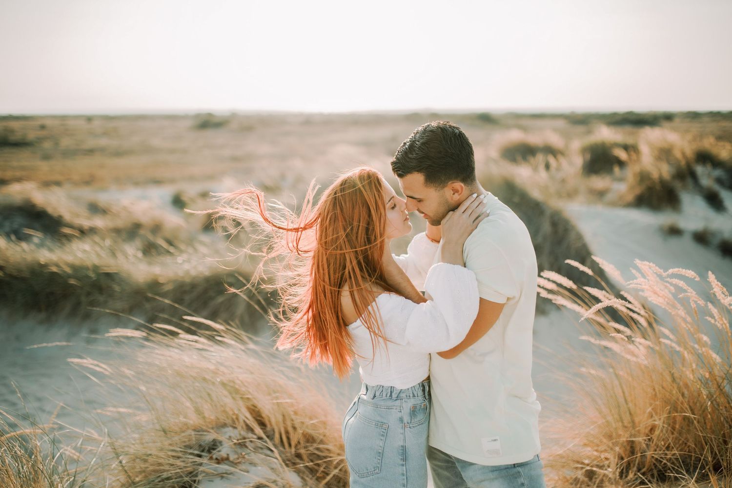 Couple sharing romantic moments in golden grass field during sunset, captured in multiple candid poses.