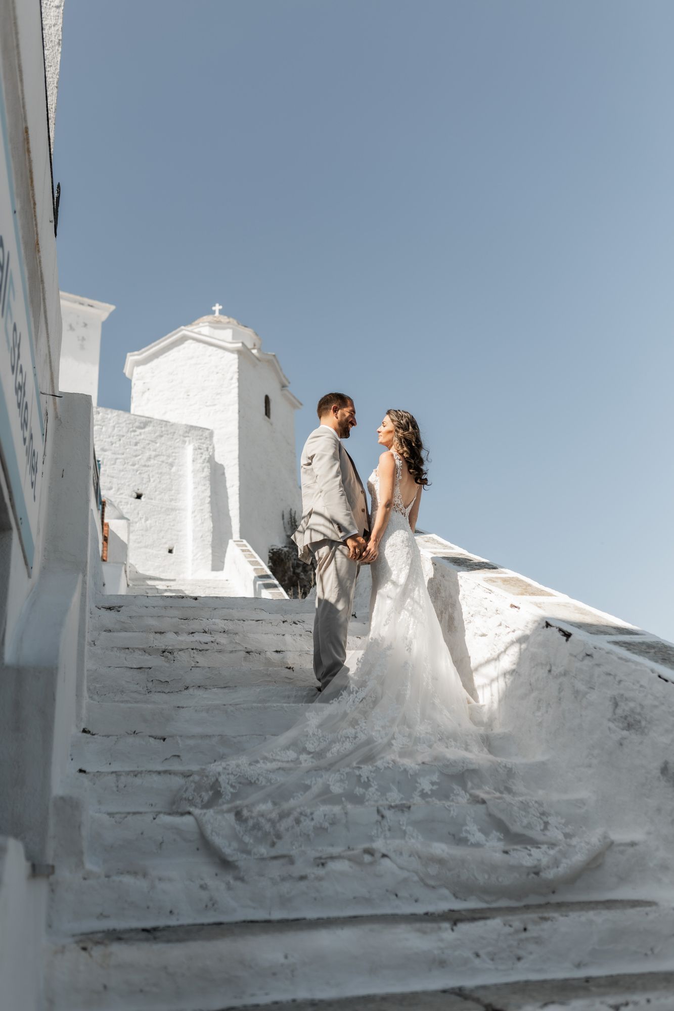 Wedding couple poses on white stone steps of Mediterranean architecture under blue sky.