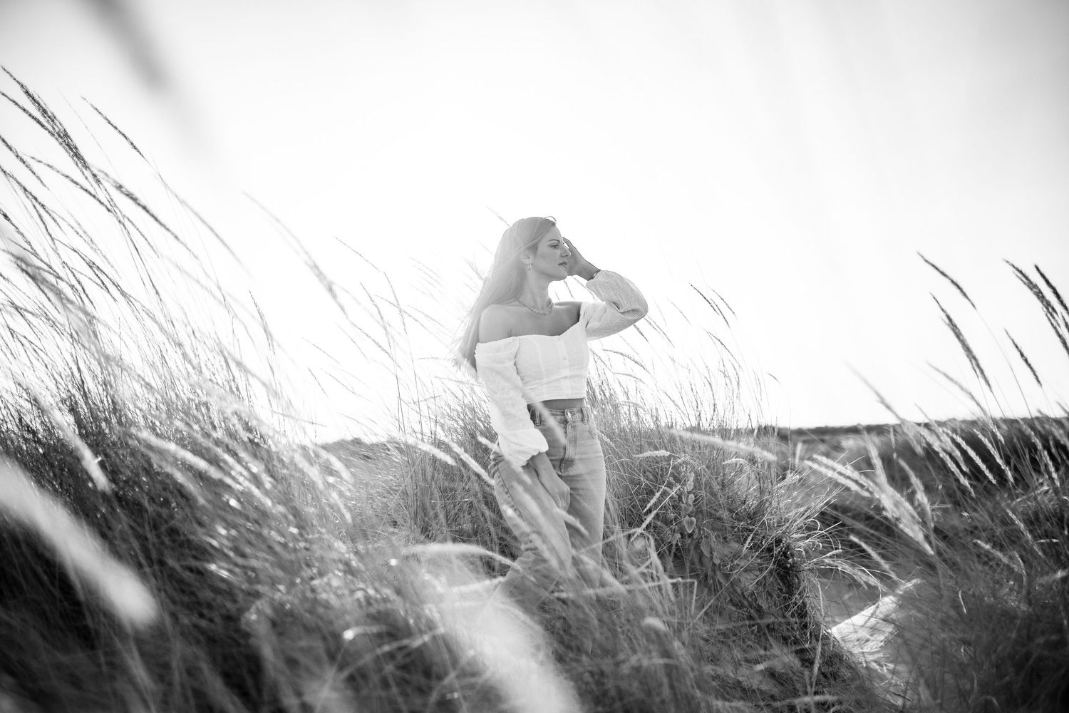 Black and white photo of a pelican perched on a grassy dune against a bright sky background.