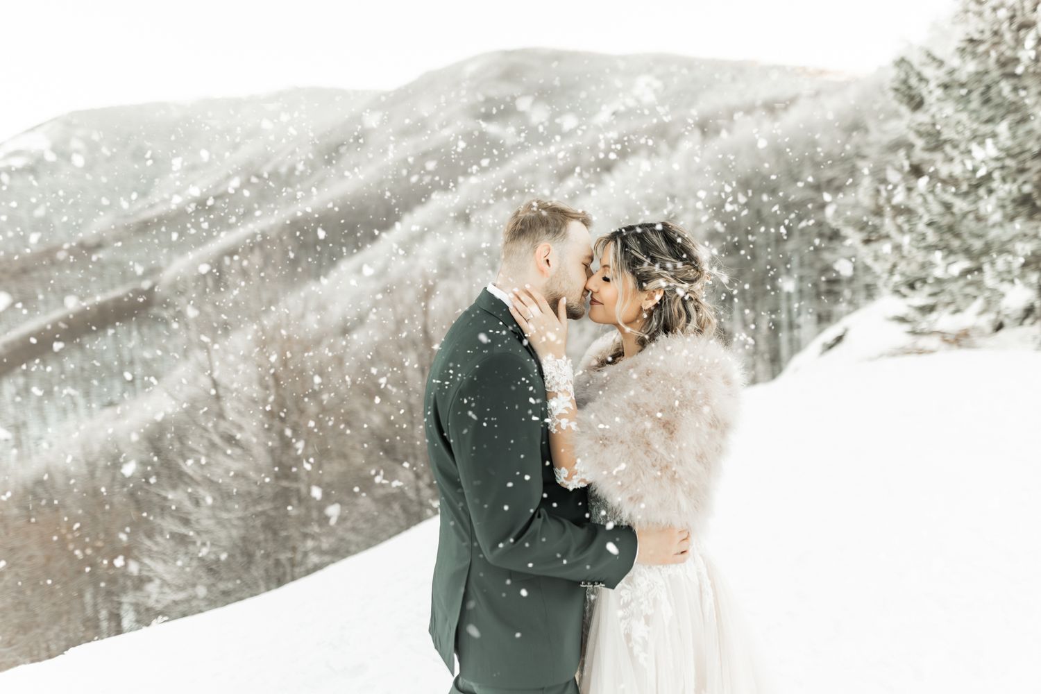 Romantic winter wedding photos with falling snow and mountain scenery.