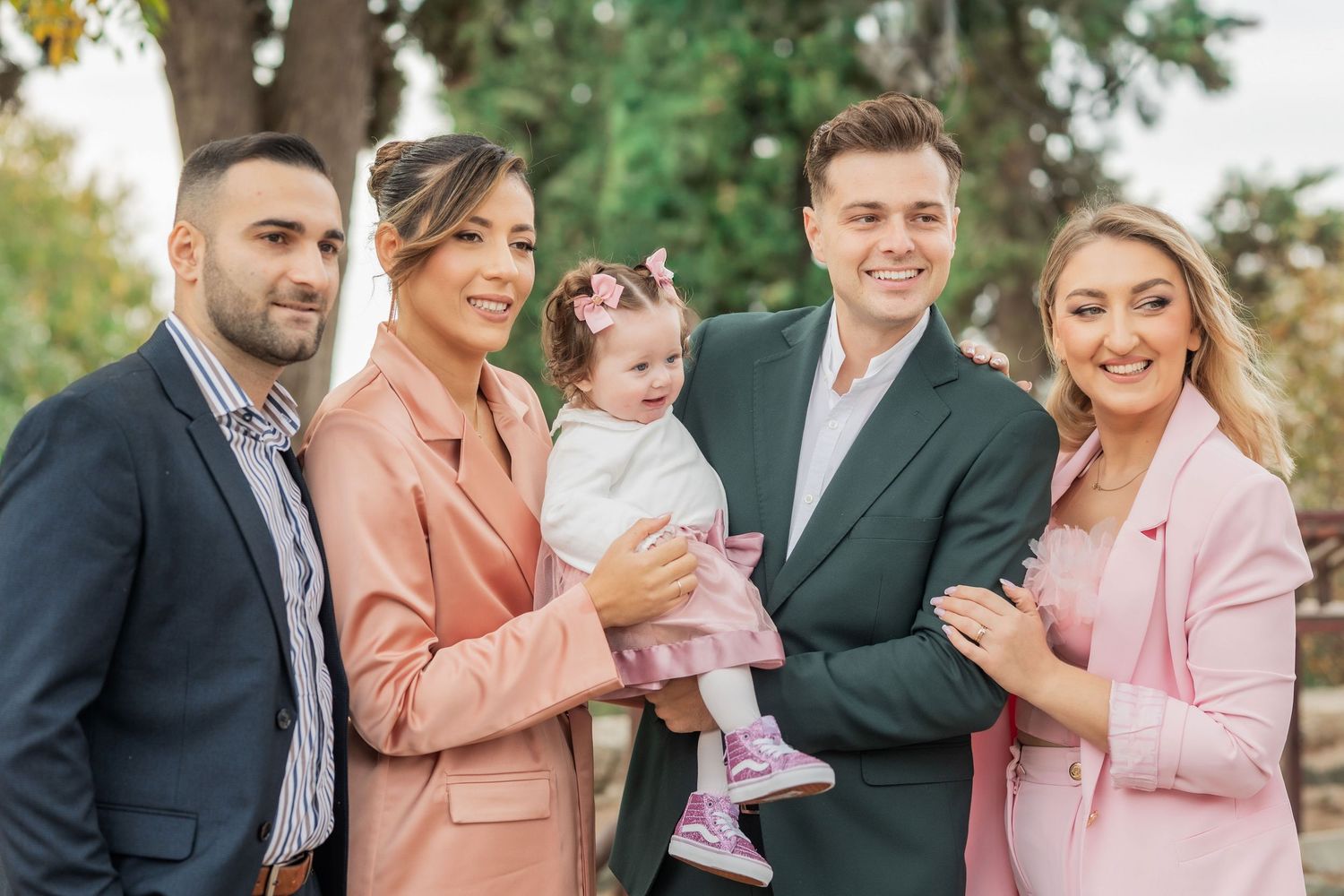 A family in coordinated pink and navy outfits poses together outdoors during a photo session in autumn.