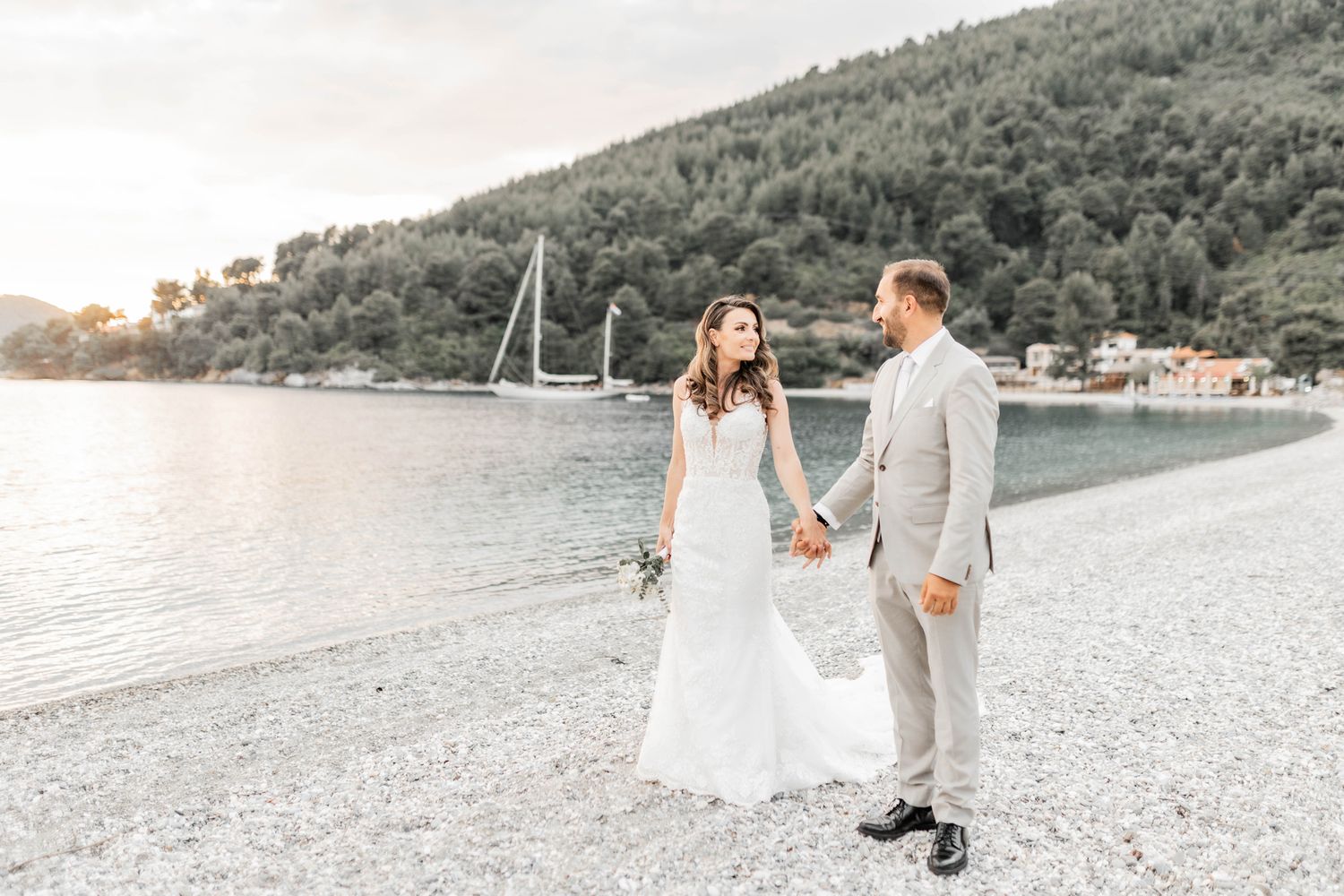 Couple poses for romantic photos on a beach with mountains in the background.
