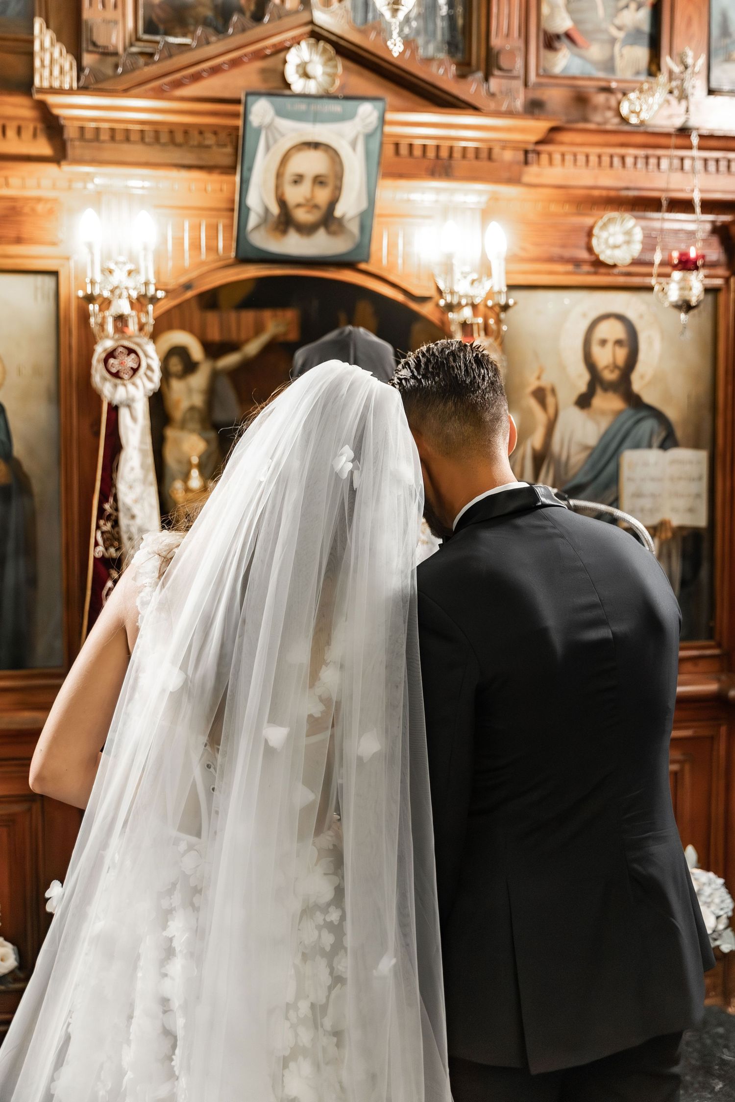 Orthodox church wedding ceremony with ornate wooden details and chandeliers.
